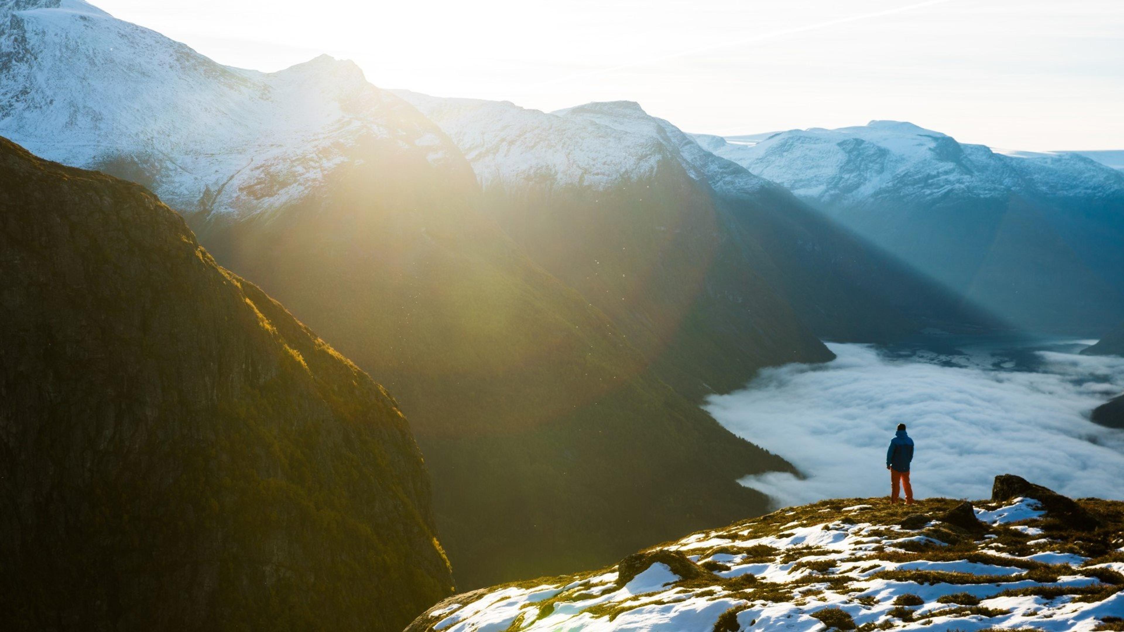 En person som ser utover snødekkede fjell med solnedgang i det fjerne