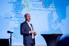 En mann på scenen står foran et verdenskart