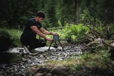 En mann som sitter på huk med en drone ute i naturen