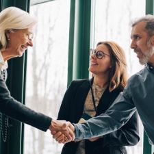 To damer og en mann som smiler og hilser på hverandre.