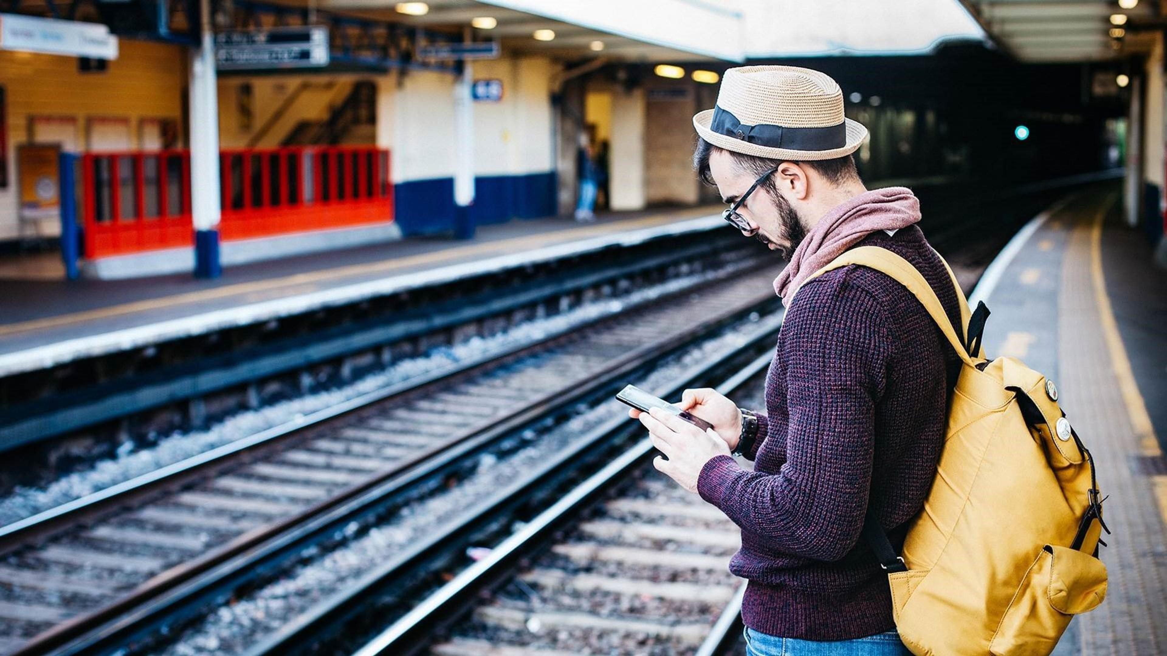 Mann på togstasjon som skriver på mobilen