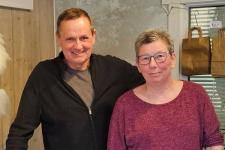 En mann og kvinne viser frem oster og tilbehør i butikken sin.