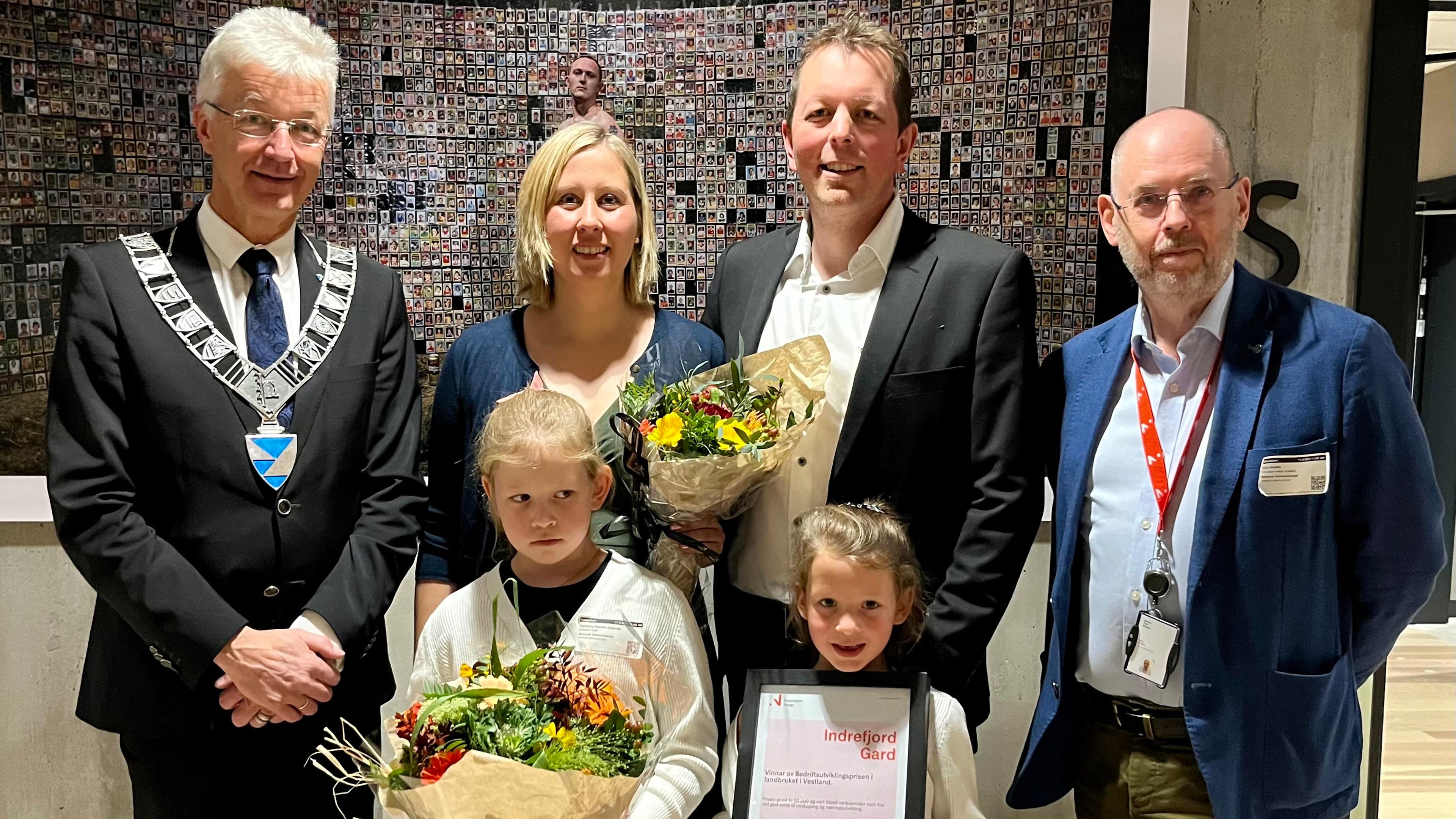 Prisvinnerne og deres to barn står med blomster og diplom ved siden av fylkesordføreren