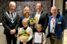 Prisvinnerne og deres to barn står med blomster og diplom ved siden av fylkesordføreren