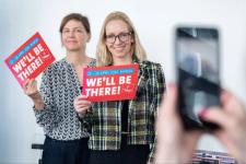 To kvinner holder opp hver sin flyer om et messearrangement