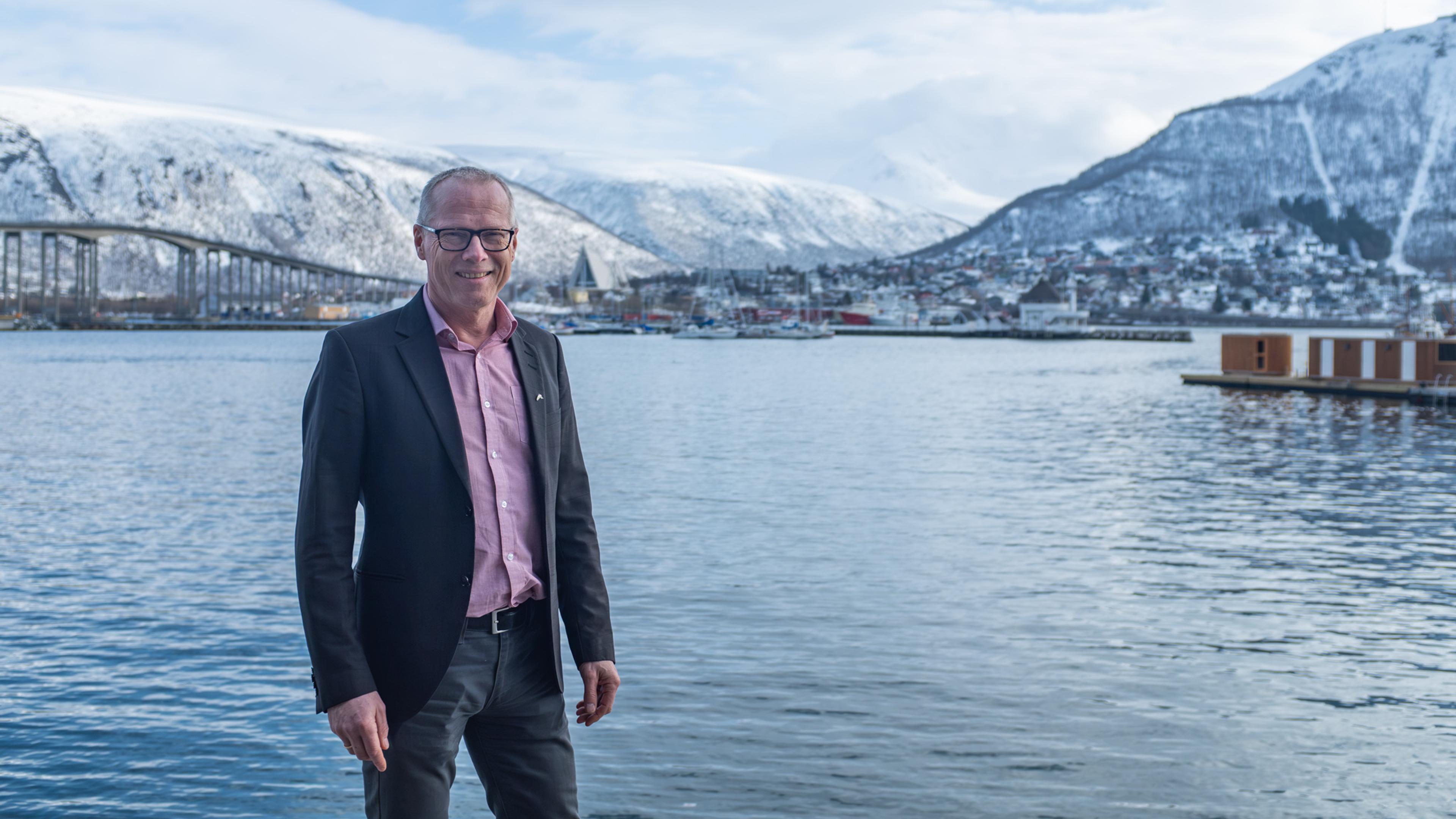 Mann smiler mot kameraet med Tromsø i bakgrunnen