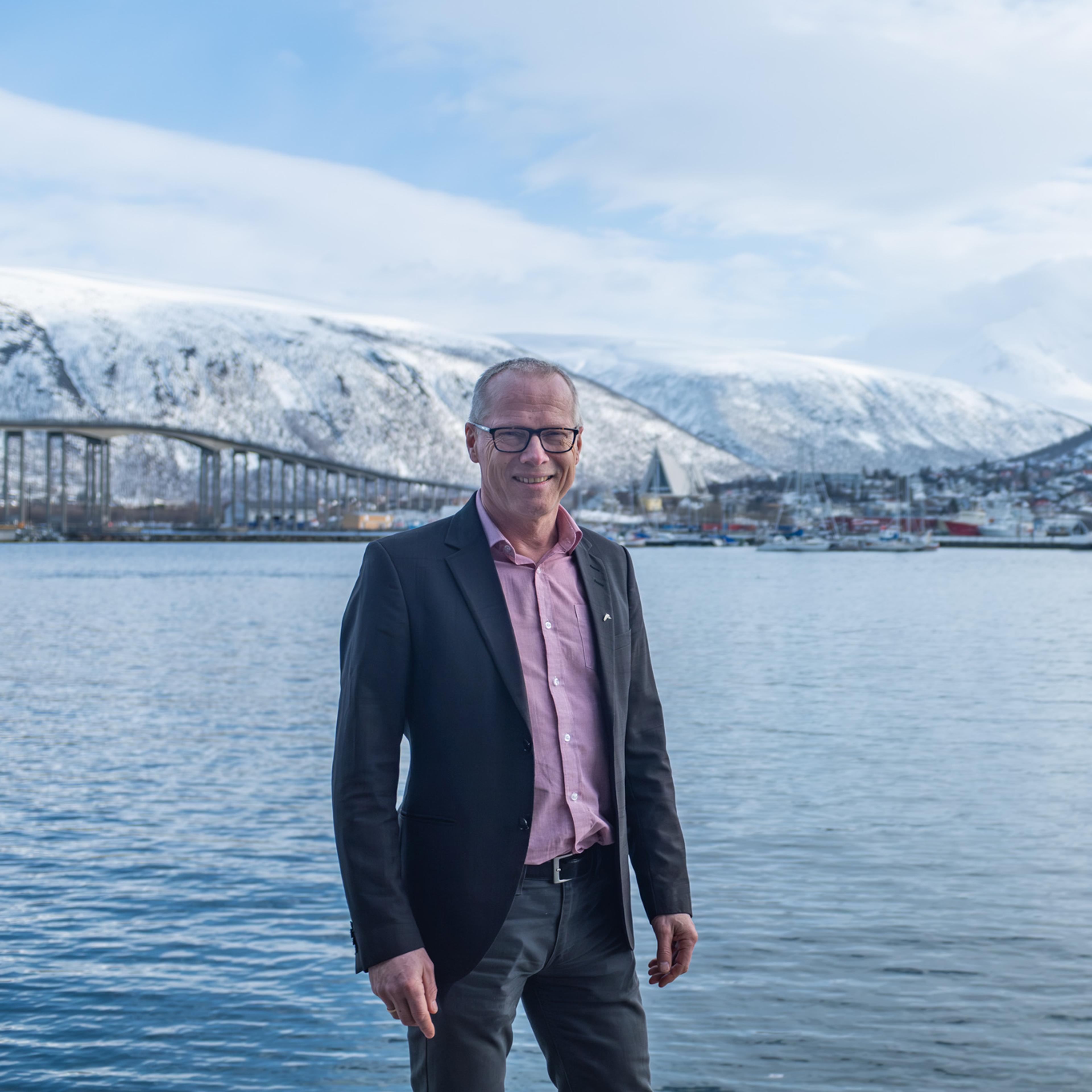 Mann smiler mot kameraet med Tromsø i bakgrunnen