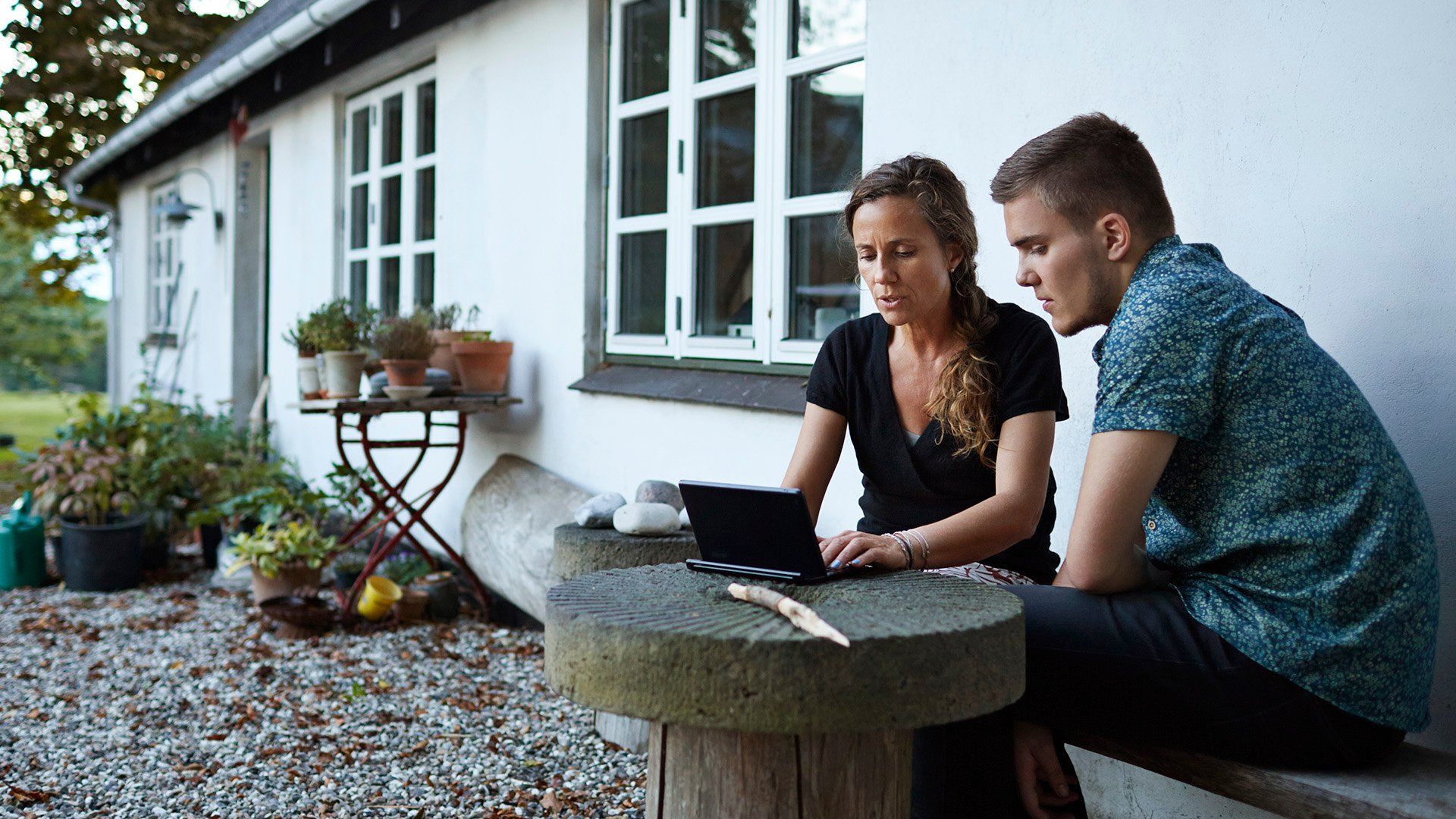 Et par som jobber på tablet på utebenk utfor et hus