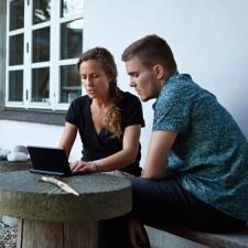 Et par som jobber på tablet på utebenk utfor et hus