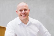 Et portrettbilde av en mann i hvit skjorte som smiler