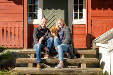 En mann og ei dame sitter på inngangstrappa til huset sitt med en hund mellom seg