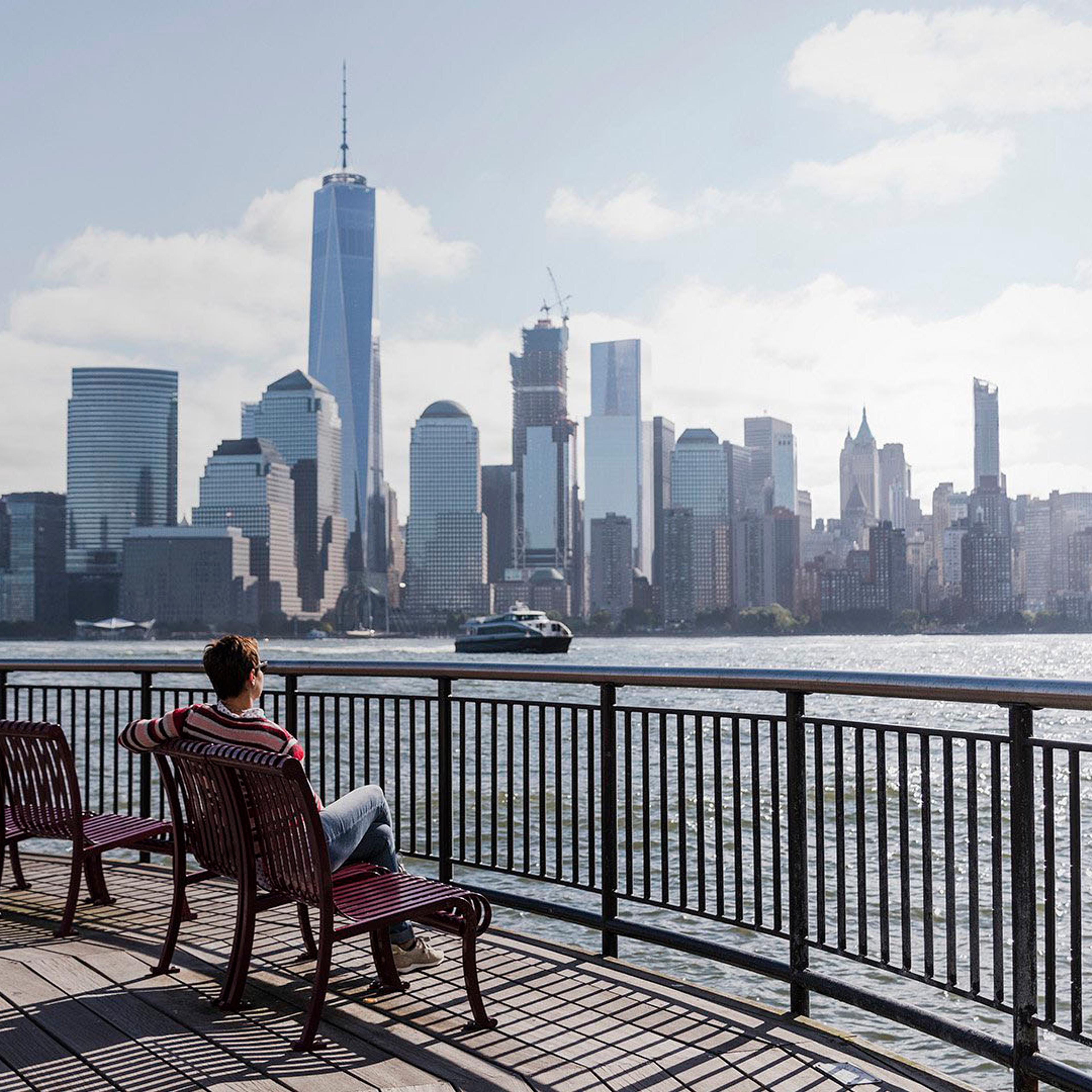 En person sitter på en benk og ser på Manhattan skyline i New York