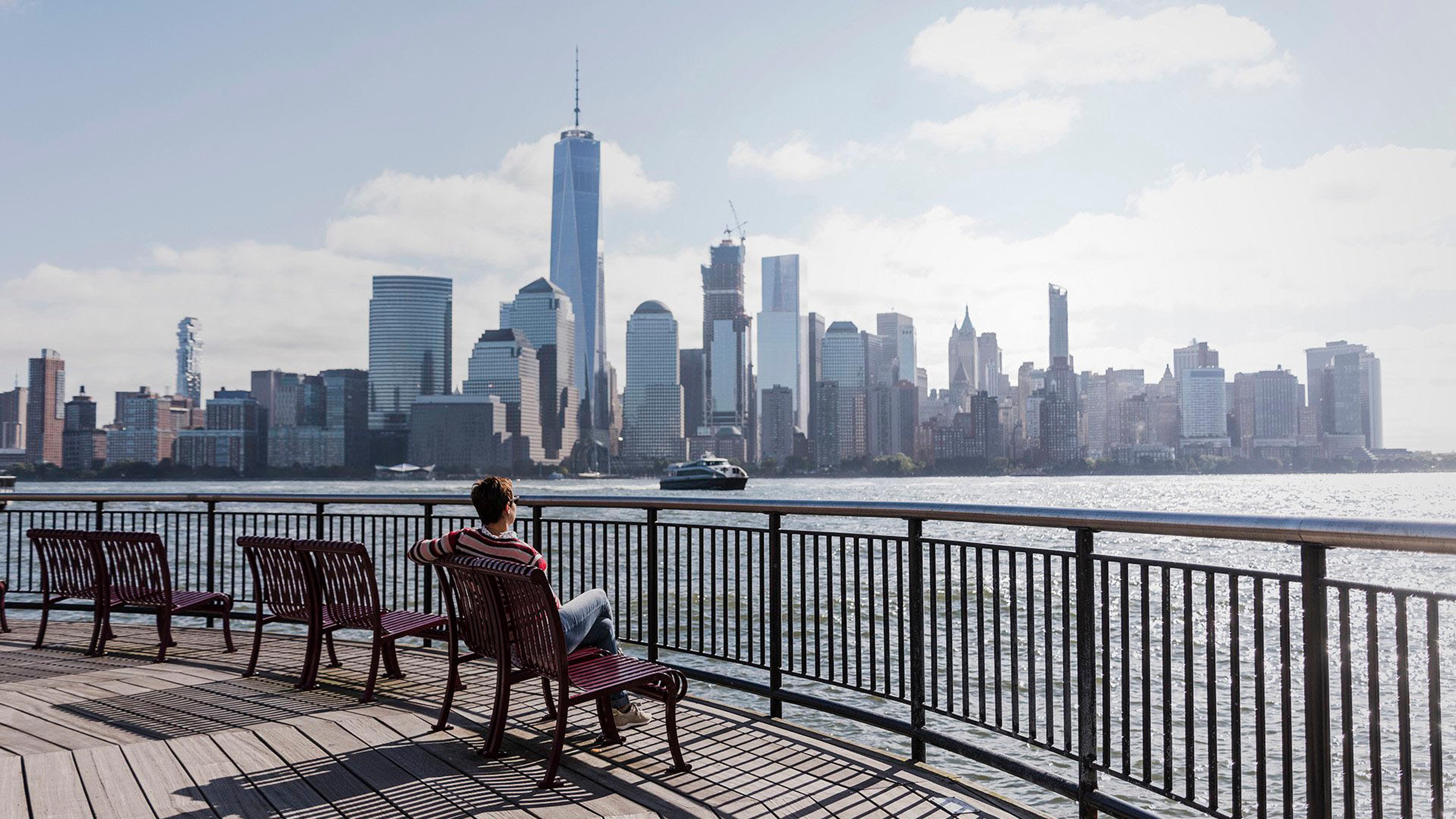 En person sitter på en benk og ser på Manhattan skyline i New York