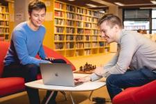 To menn sitter i et bibliotek og ser på en datamaskin