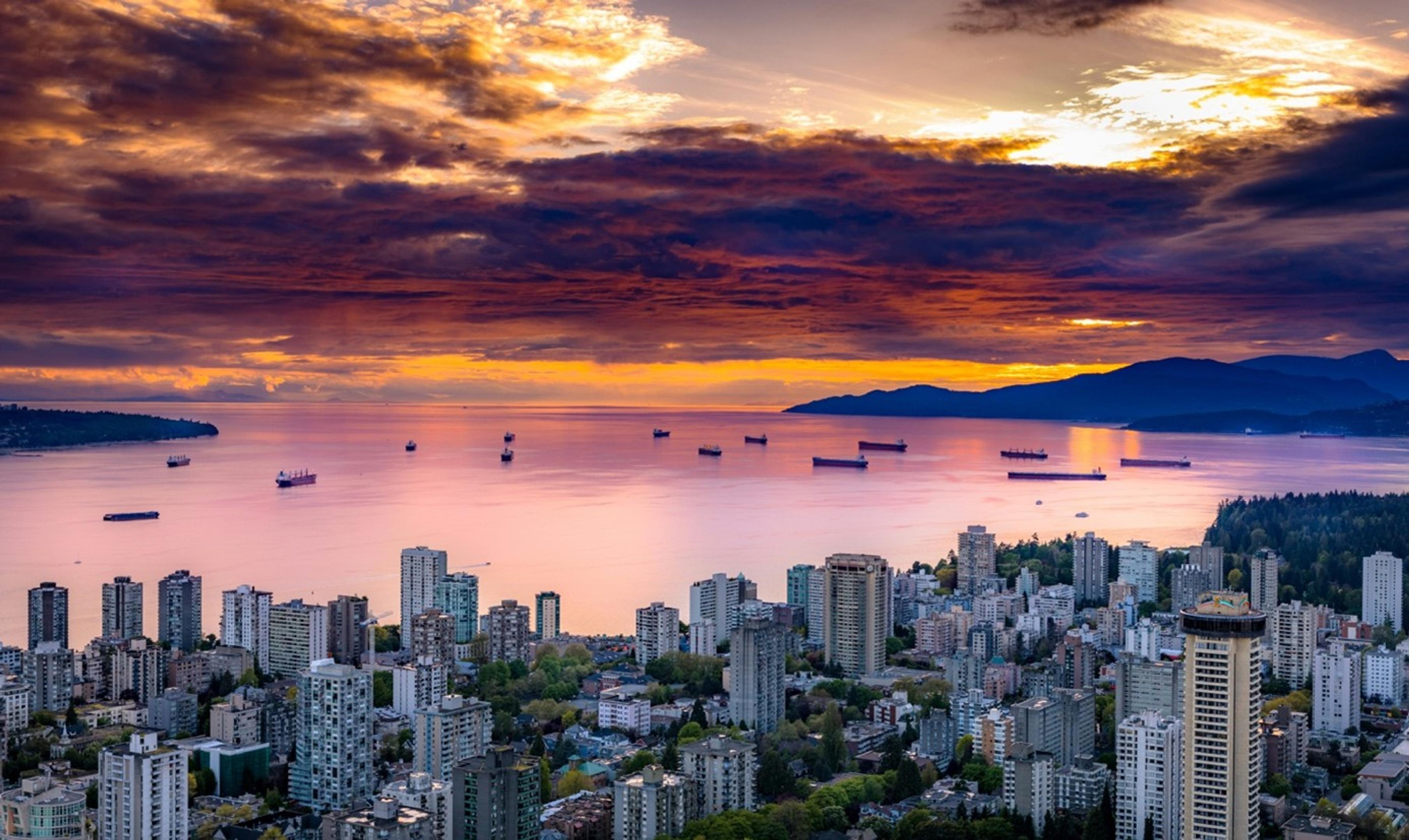 Solnedgang farger himmelen gul og lilla over Vancouver og havet utenfor byen