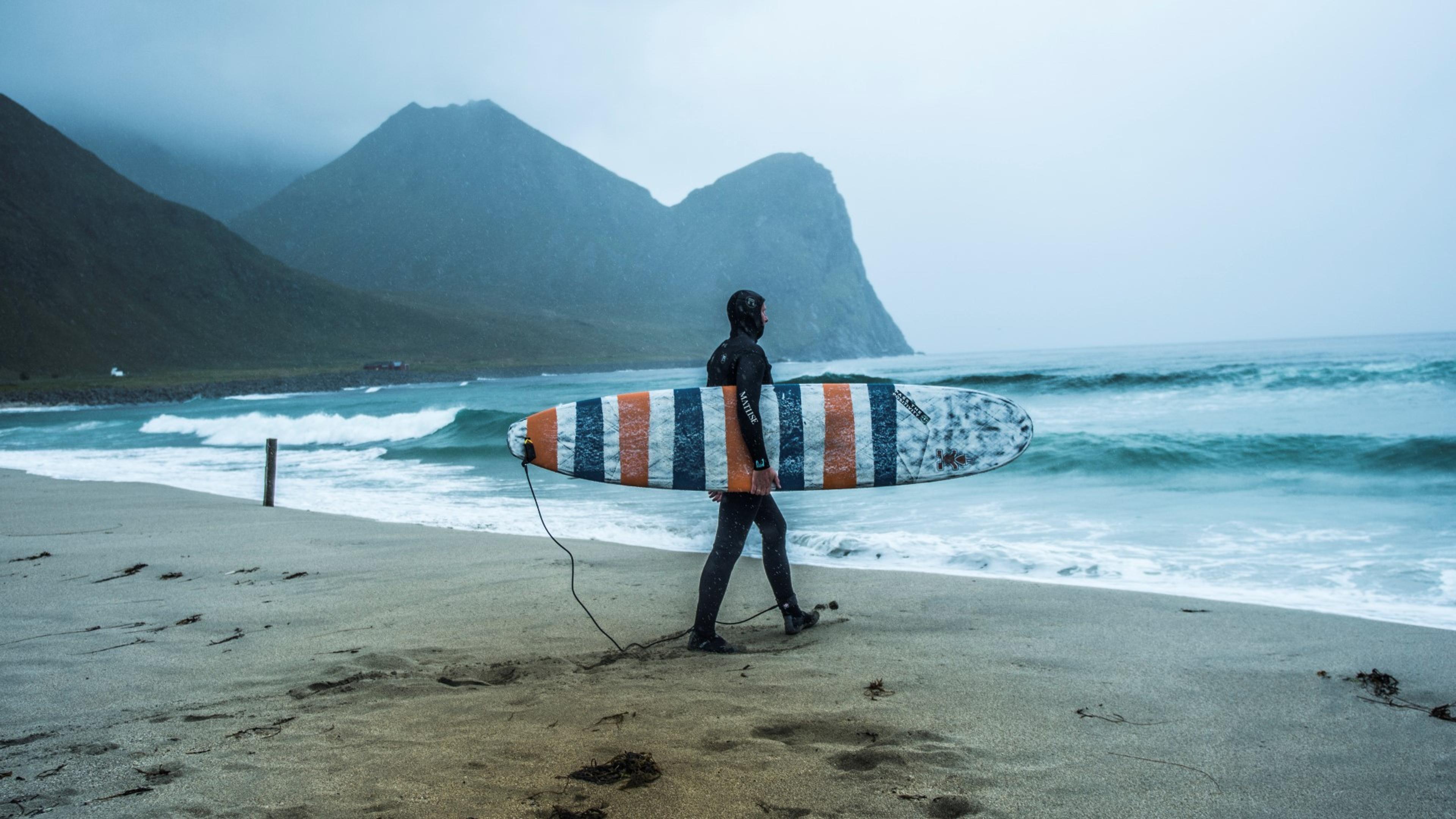 En person med surfebrett på vei ut i havet i Lofoten