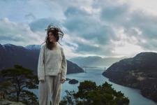 Dame som står på et utsiktspunkt ved en fjord i Norge og vinden som blåser i håret