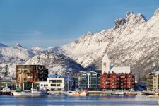 Brygge i Lofoten med snødekte fjell i bakgrunnen. Det er sol og fint vær