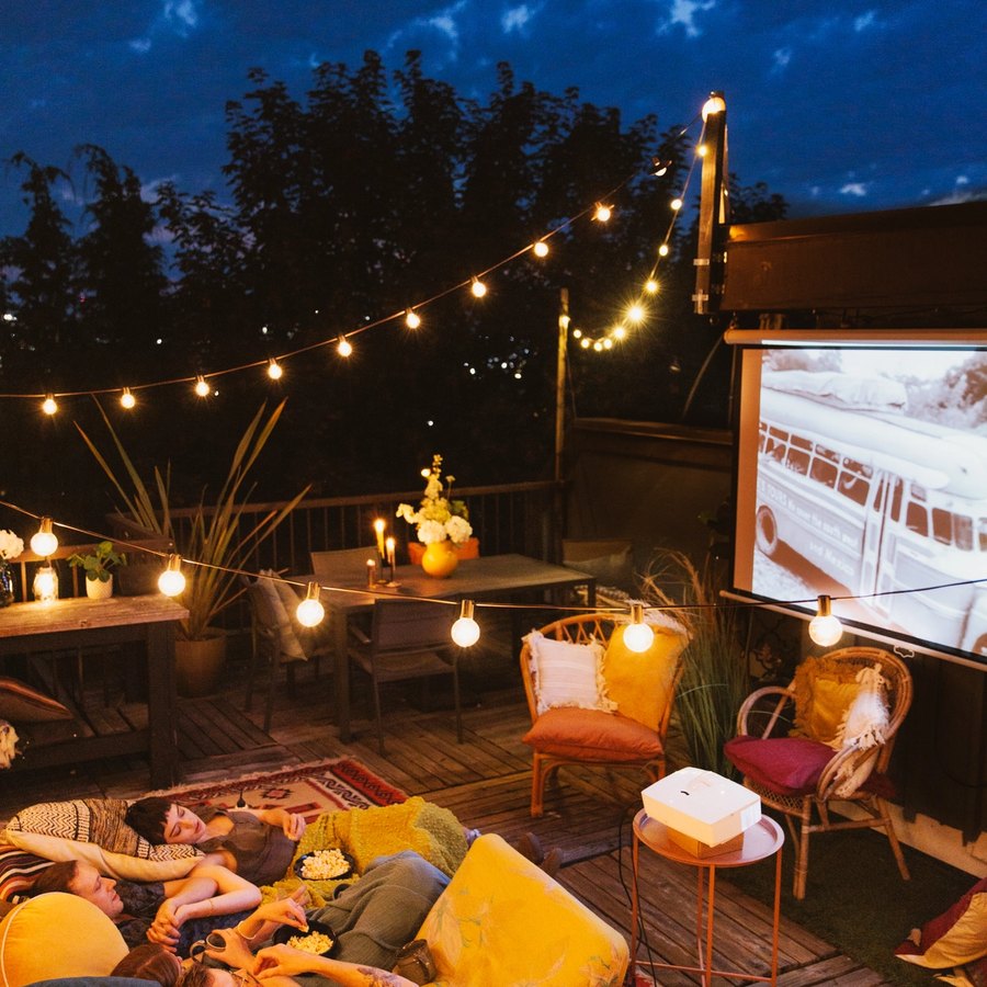 Backyard movie night with string lights, pillows, and a projector screen.