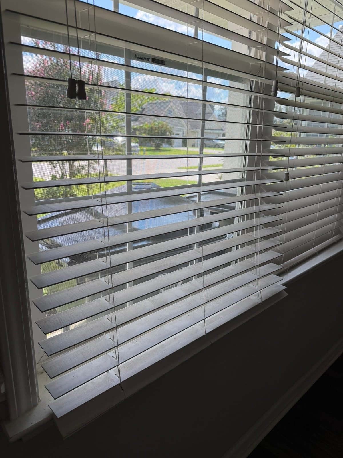 White wooden blinds on a window looking out onto a street.