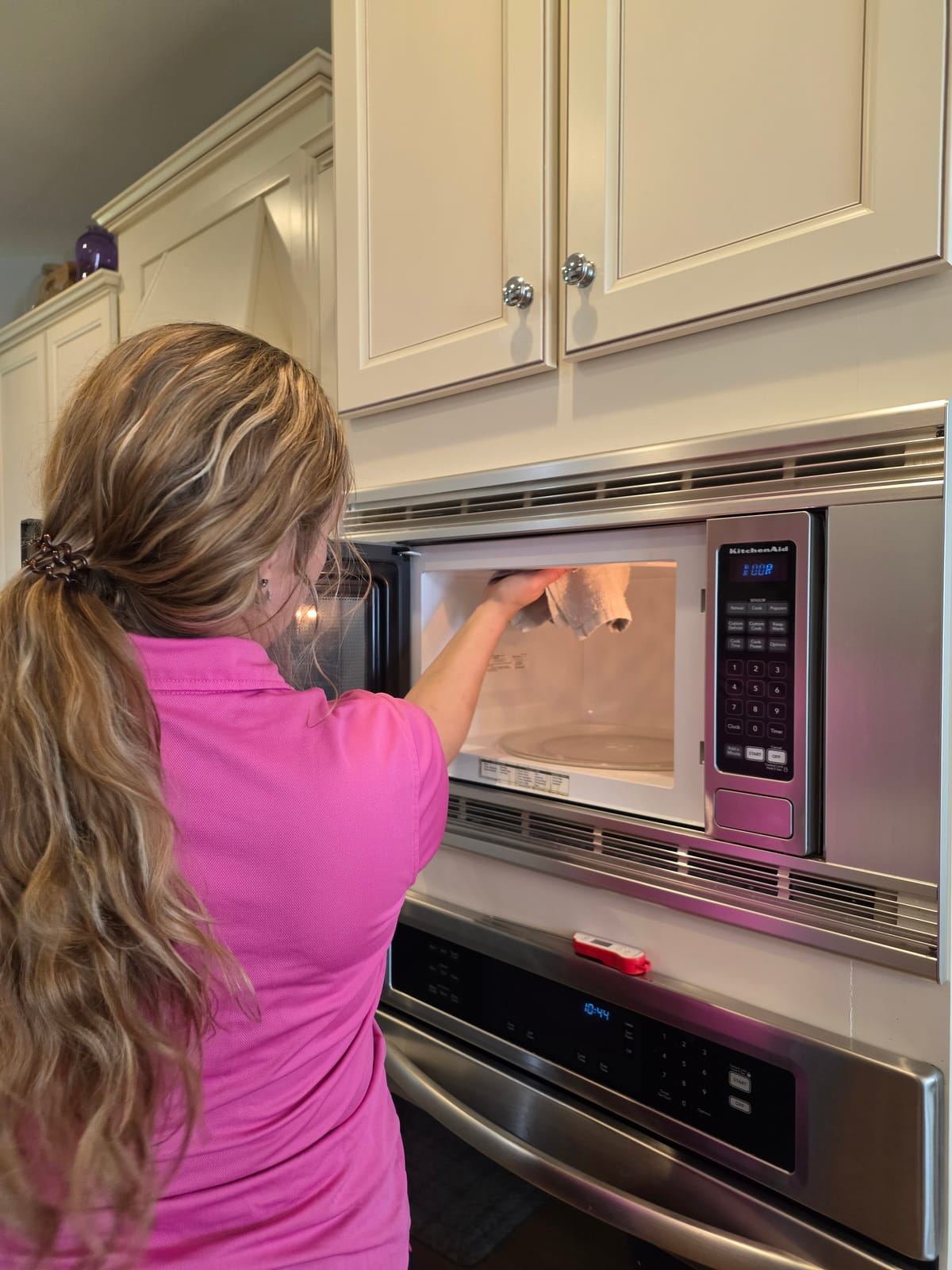A cleaner in a pink polo wiping the inside of a built-in microwave.