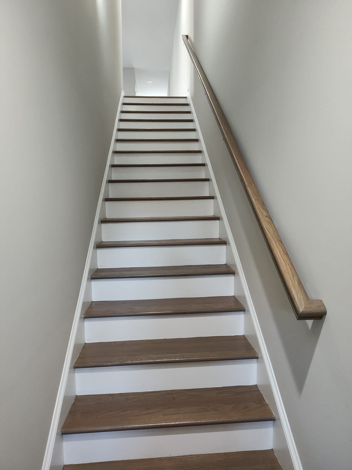 An empty staircase with white risers, wood treads and a handrail.