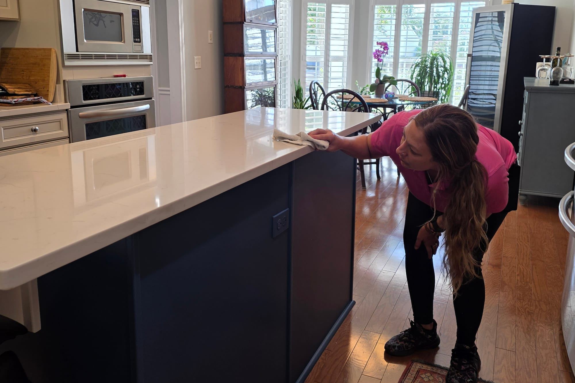 A cleaner in a pink polo wiping a white kitchen island counter.