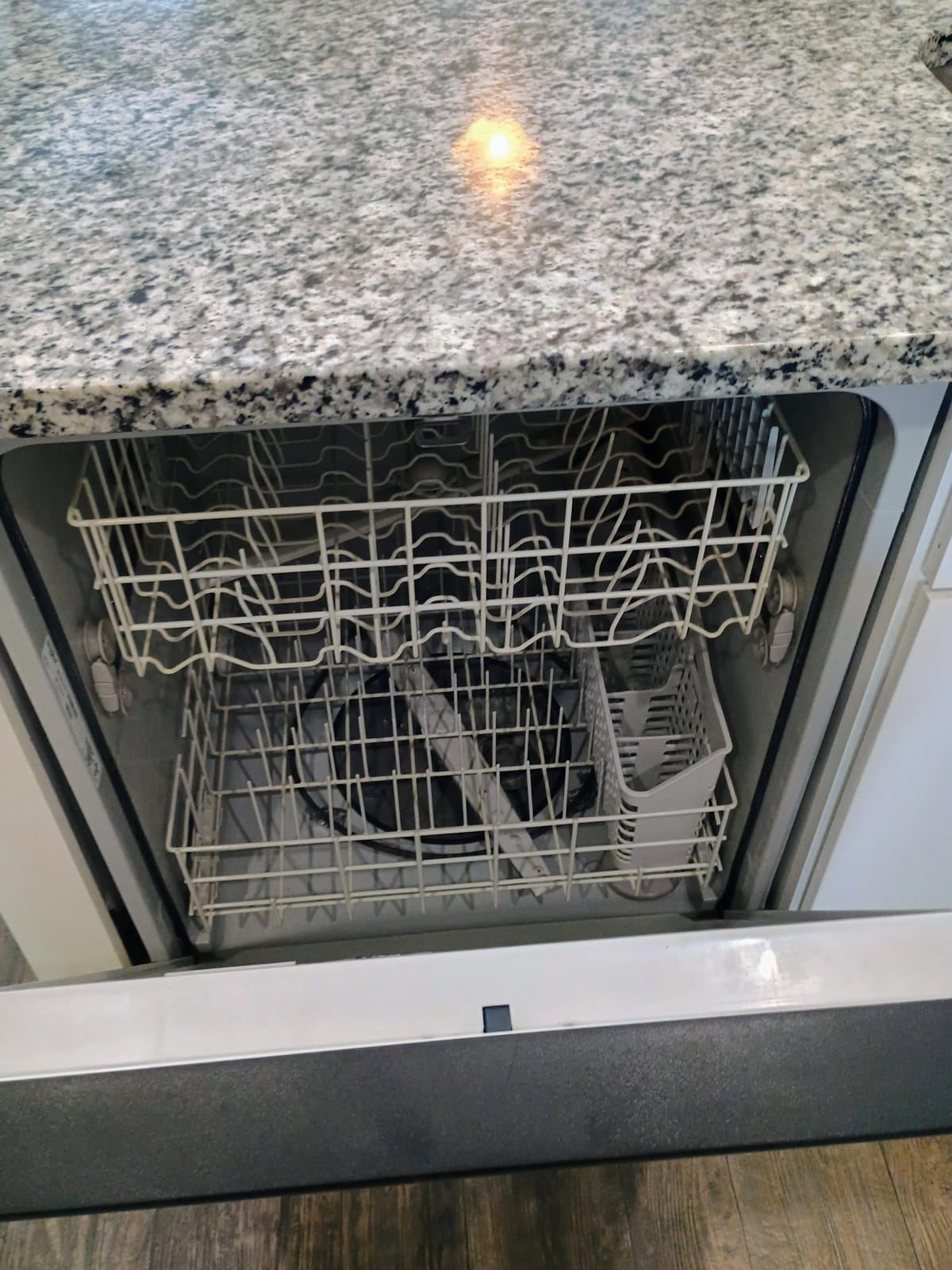 An open, empty dishwasher with a clean interior below a granite counter.