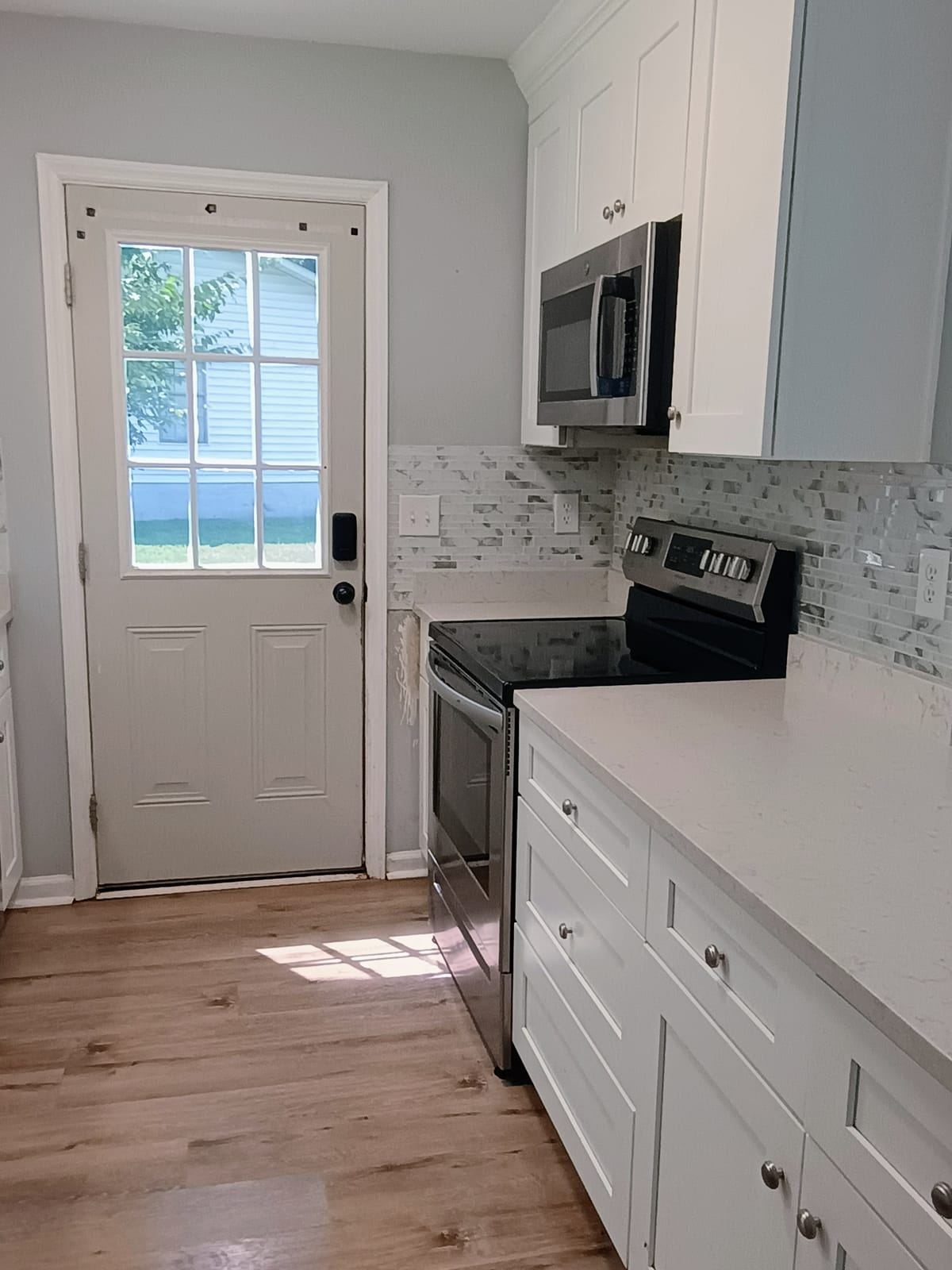 An empty kitchen with white cabinets, a stainless range and a back door.