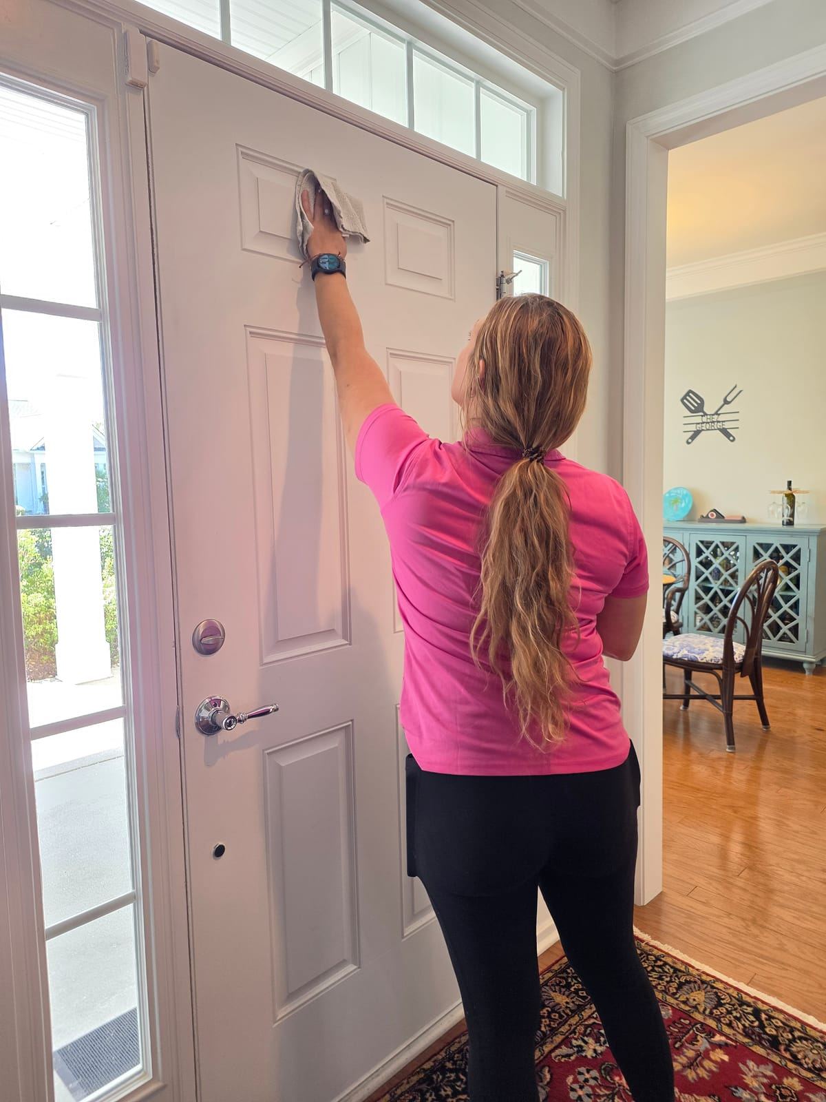A cleaner in a pink polo wiping the inside of a front door.