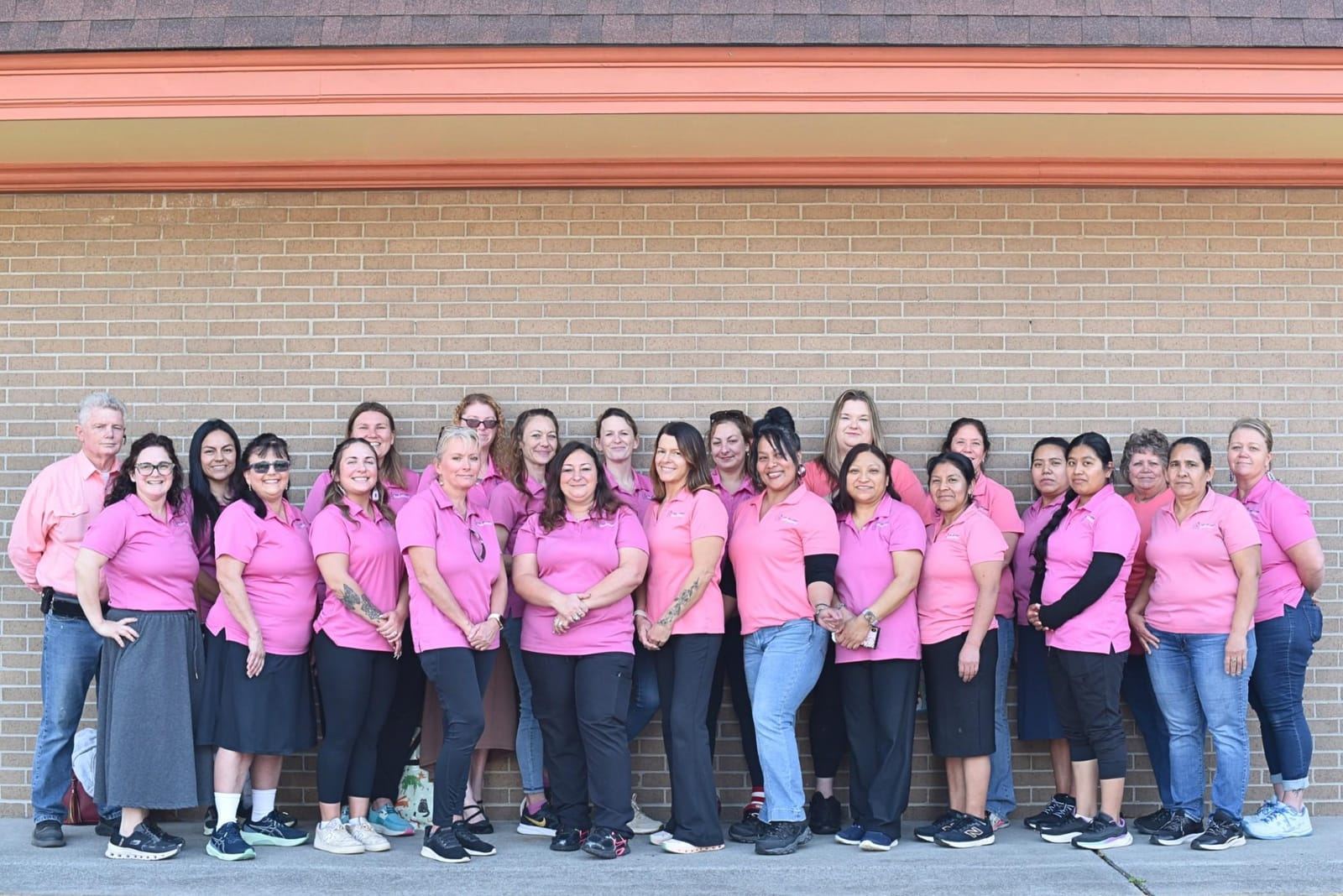 A large group of staff in pink polos standing in front of a brick wall.