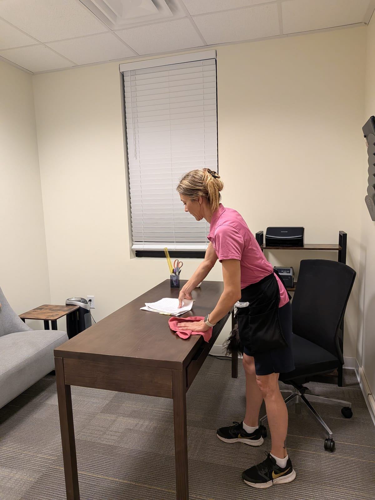 A cleaner in a pink polo wiping down an office desk.
