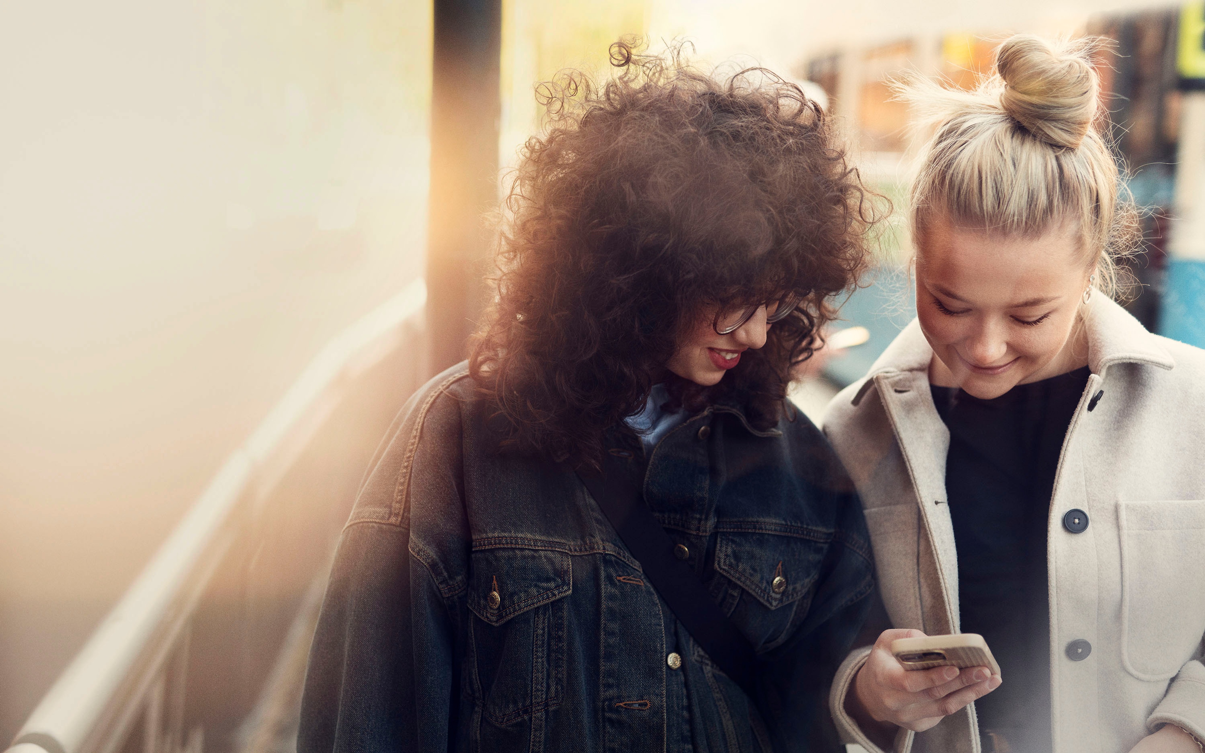 Two women beside each other looking at at phone in a city setting