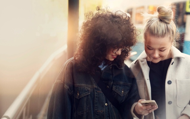 Two women beside each other looking at at phone in a city setting