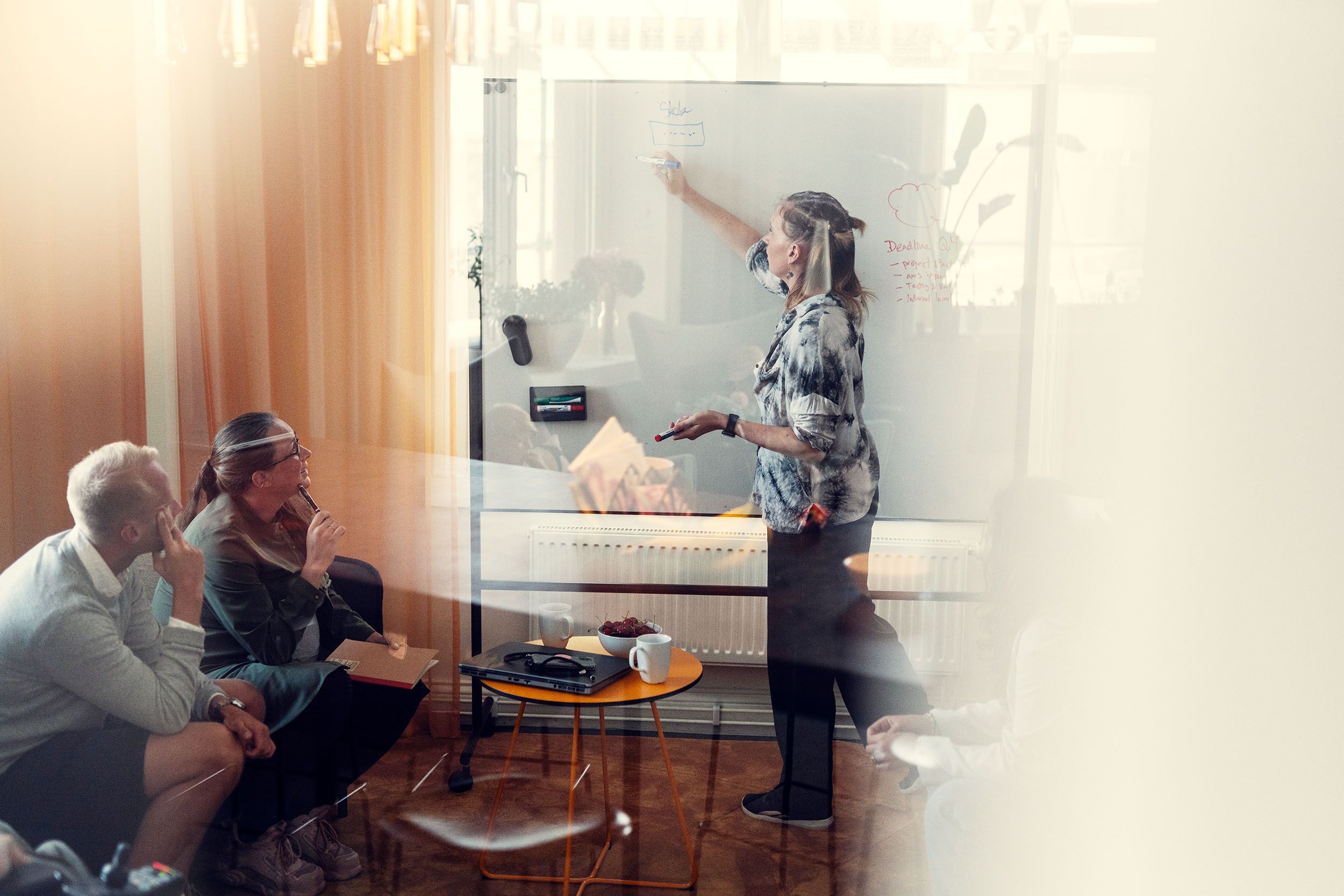 Two people looking at a woman who is writing on a whiteboard