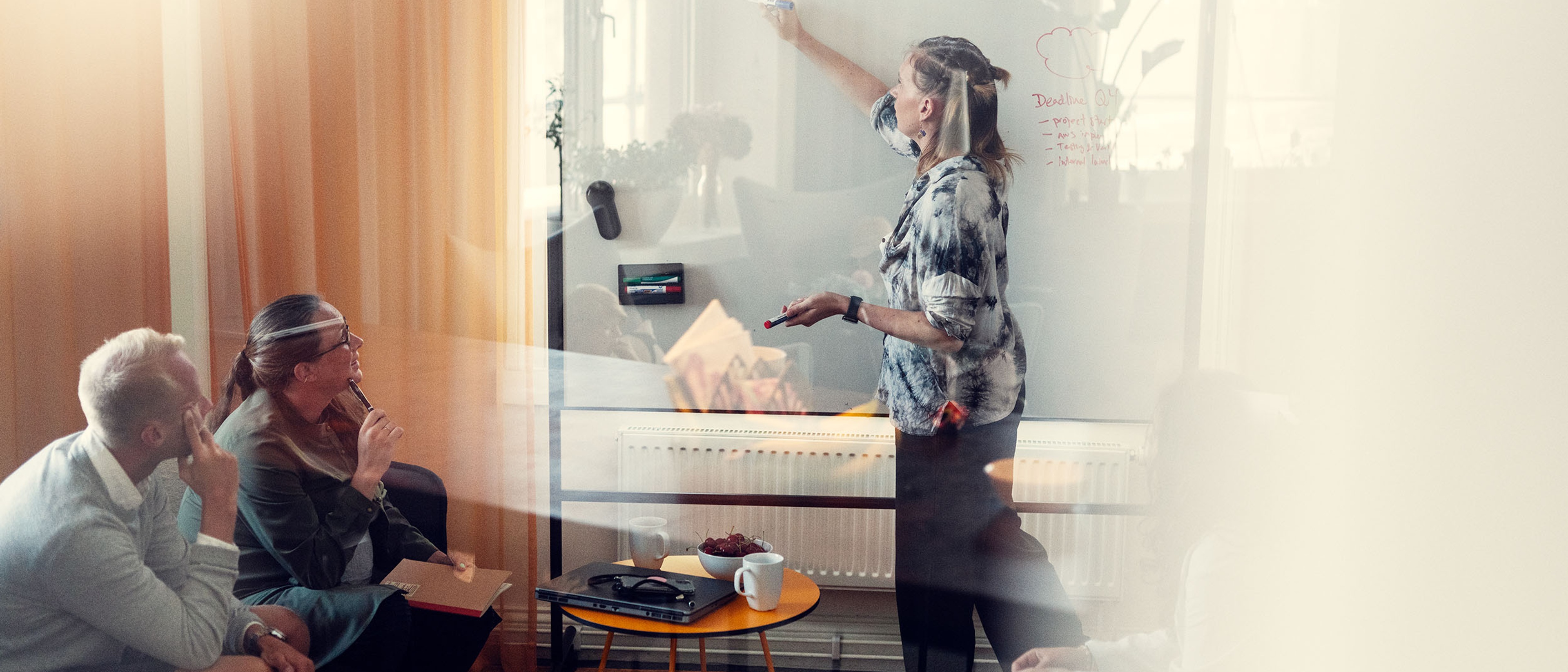 Två personer som tittar på en kvinna som skriver på en whiteboard