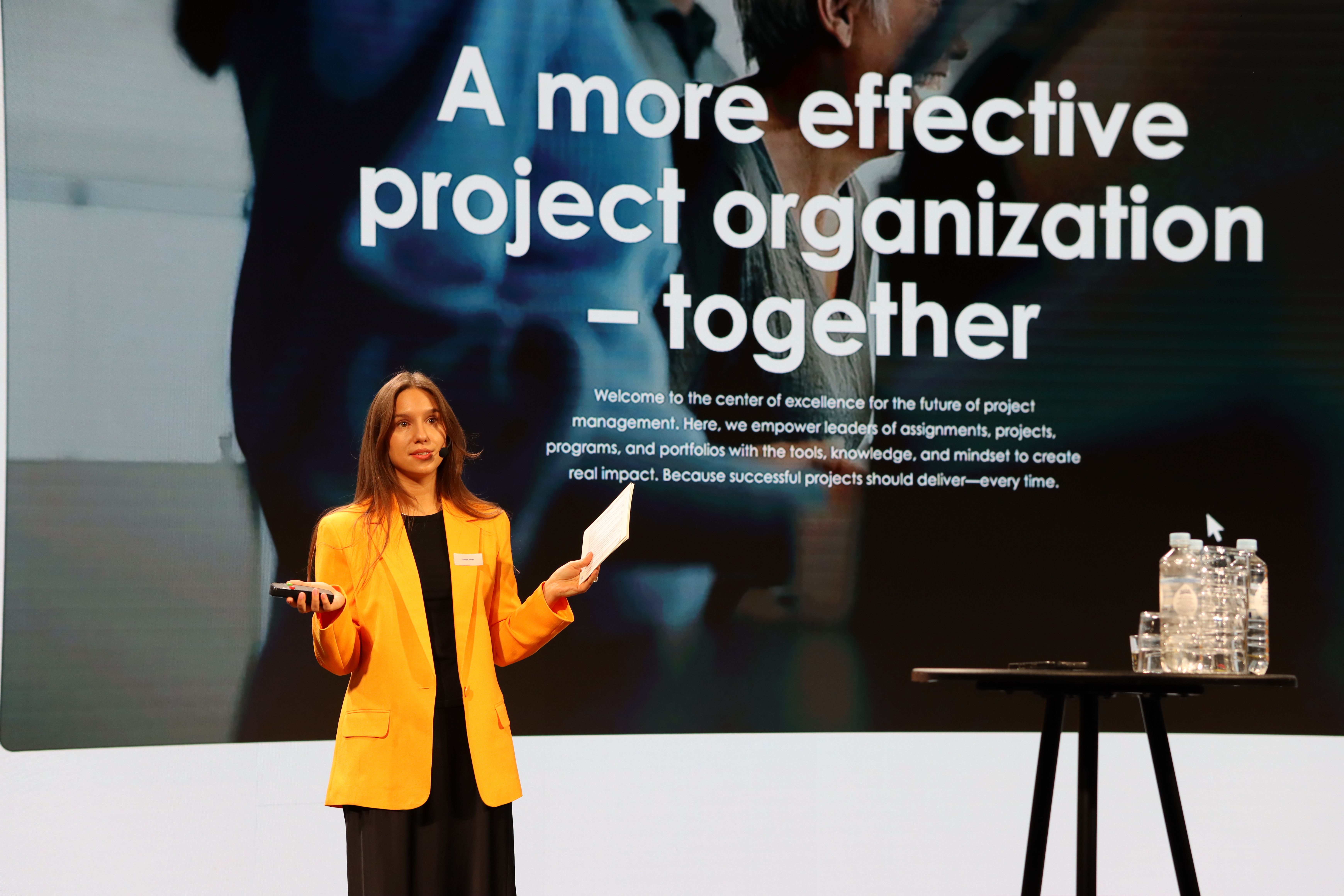 A woman in an orange jacket presenting in front of a screen
