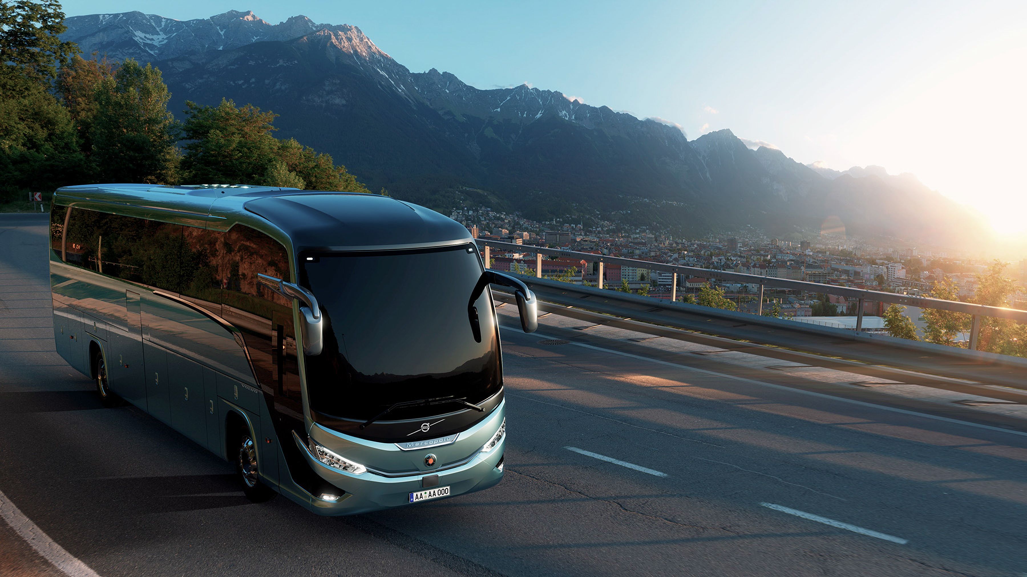 Modern bus driving along a mountain road overlooking a city at sunset.