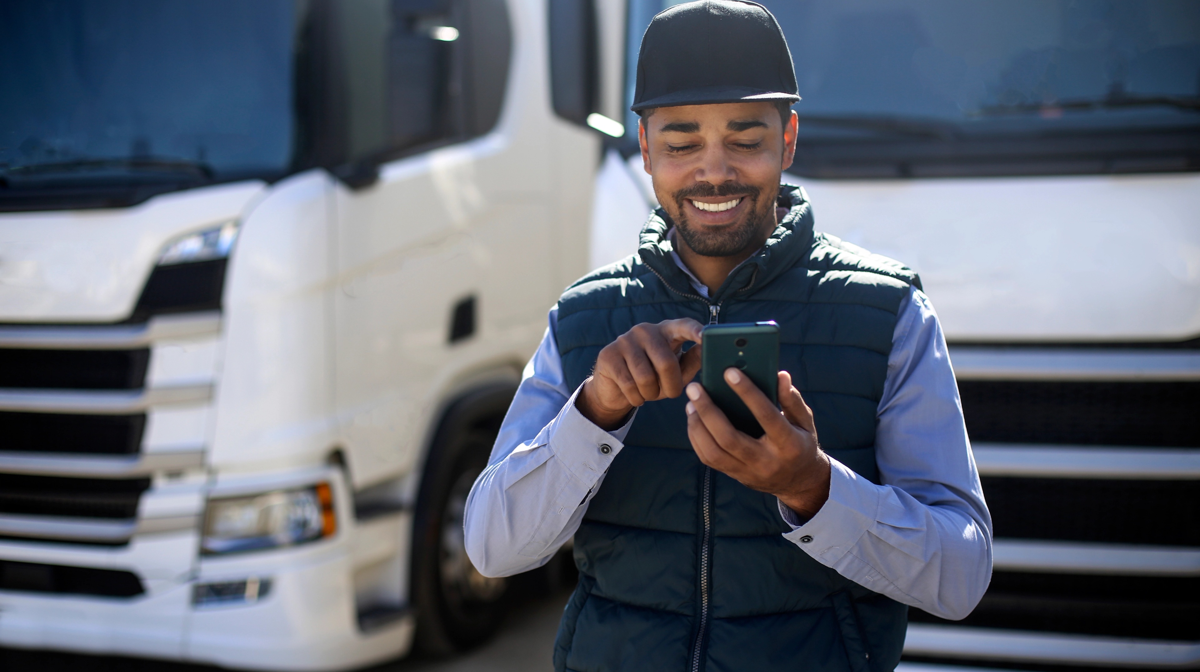 A man standing in front of two trucks at looking at a phone.