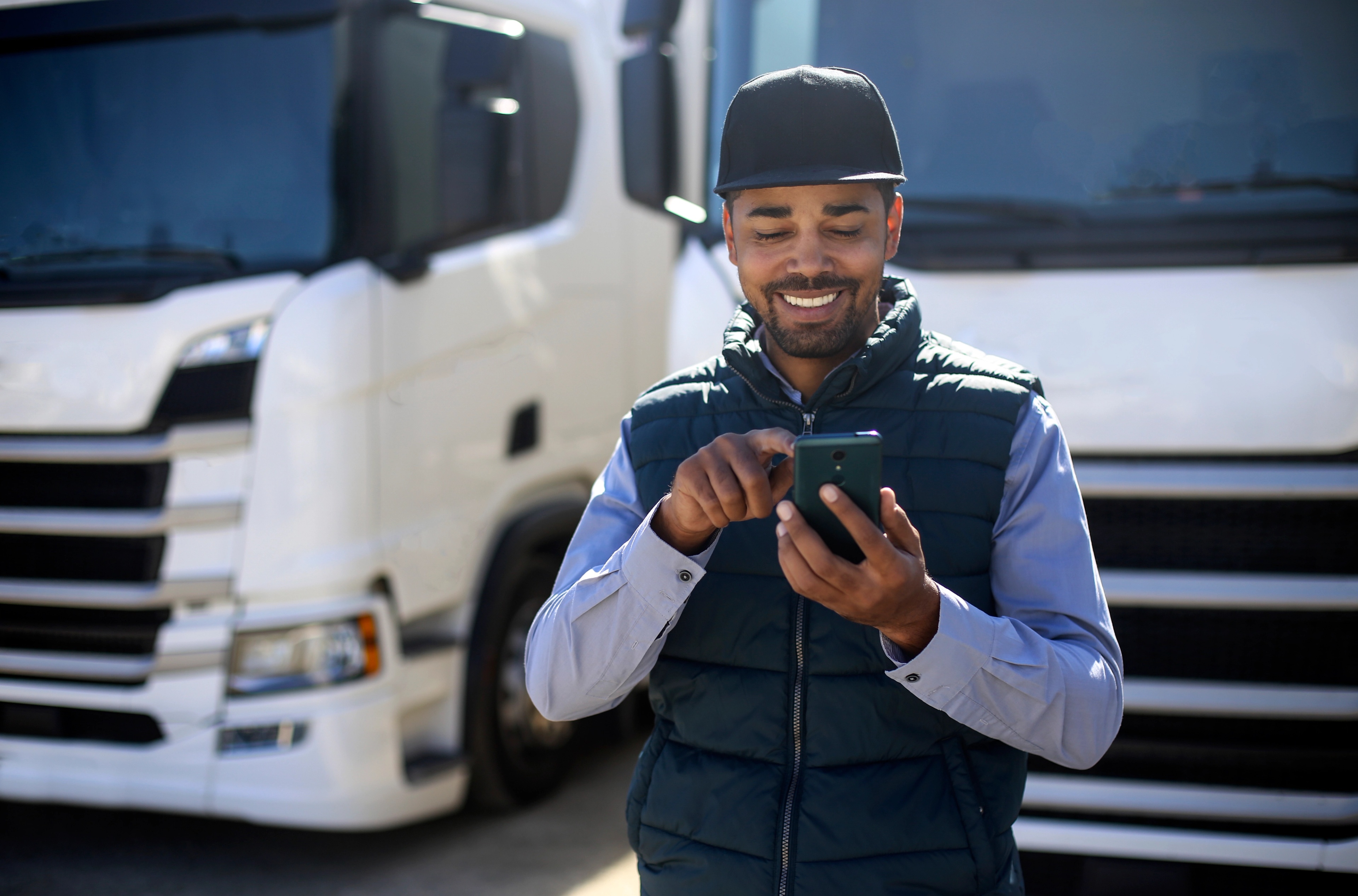 Um homem em pé em frente a dois caminhões olhando para um telefone.