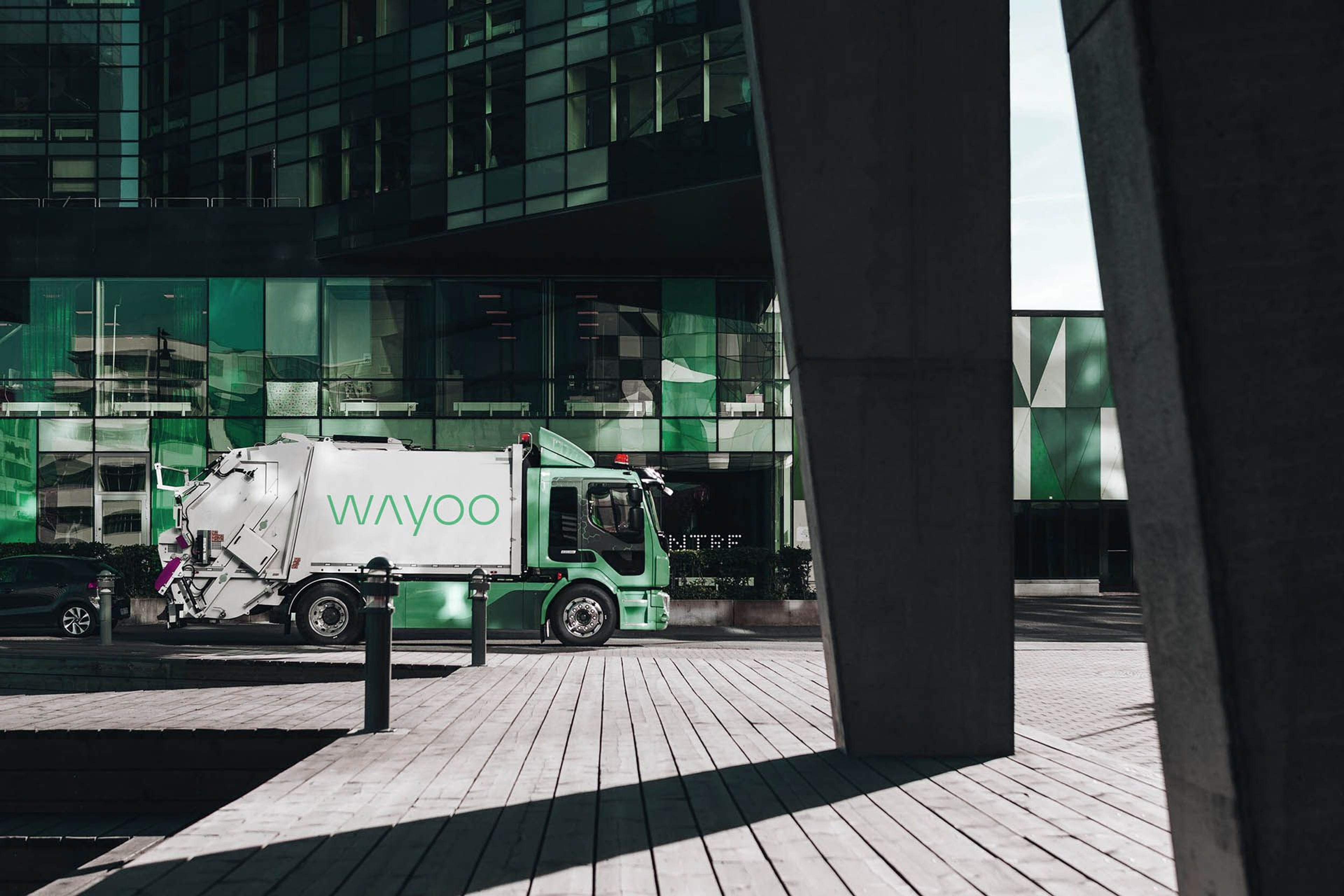 Waste collection truck parked outside a modern building with green-tinted glass facade.