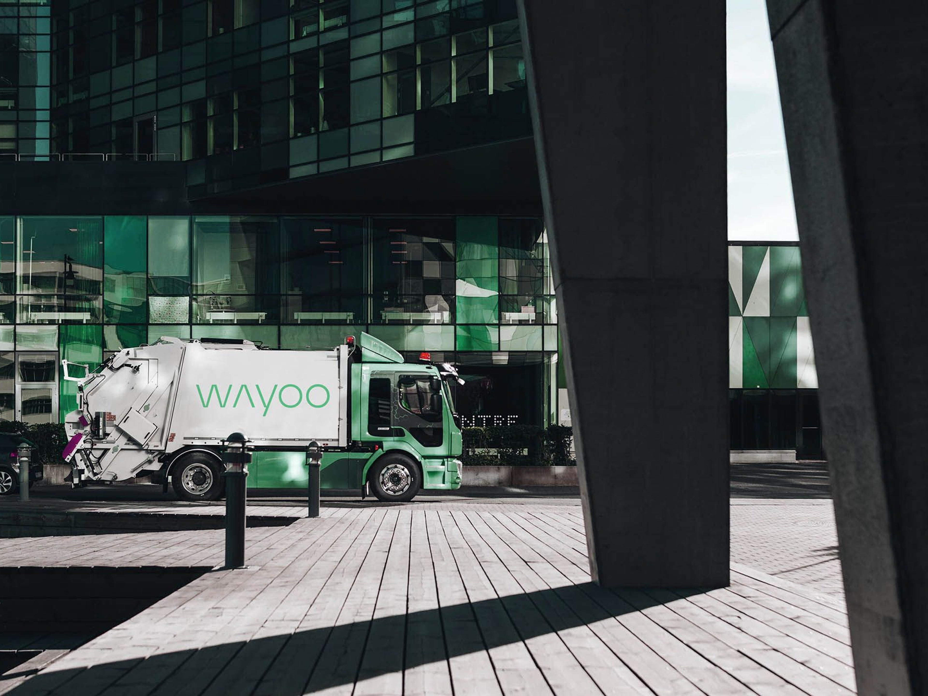 Waste collection truck parked outside a modern building with green-tinted glass facade.