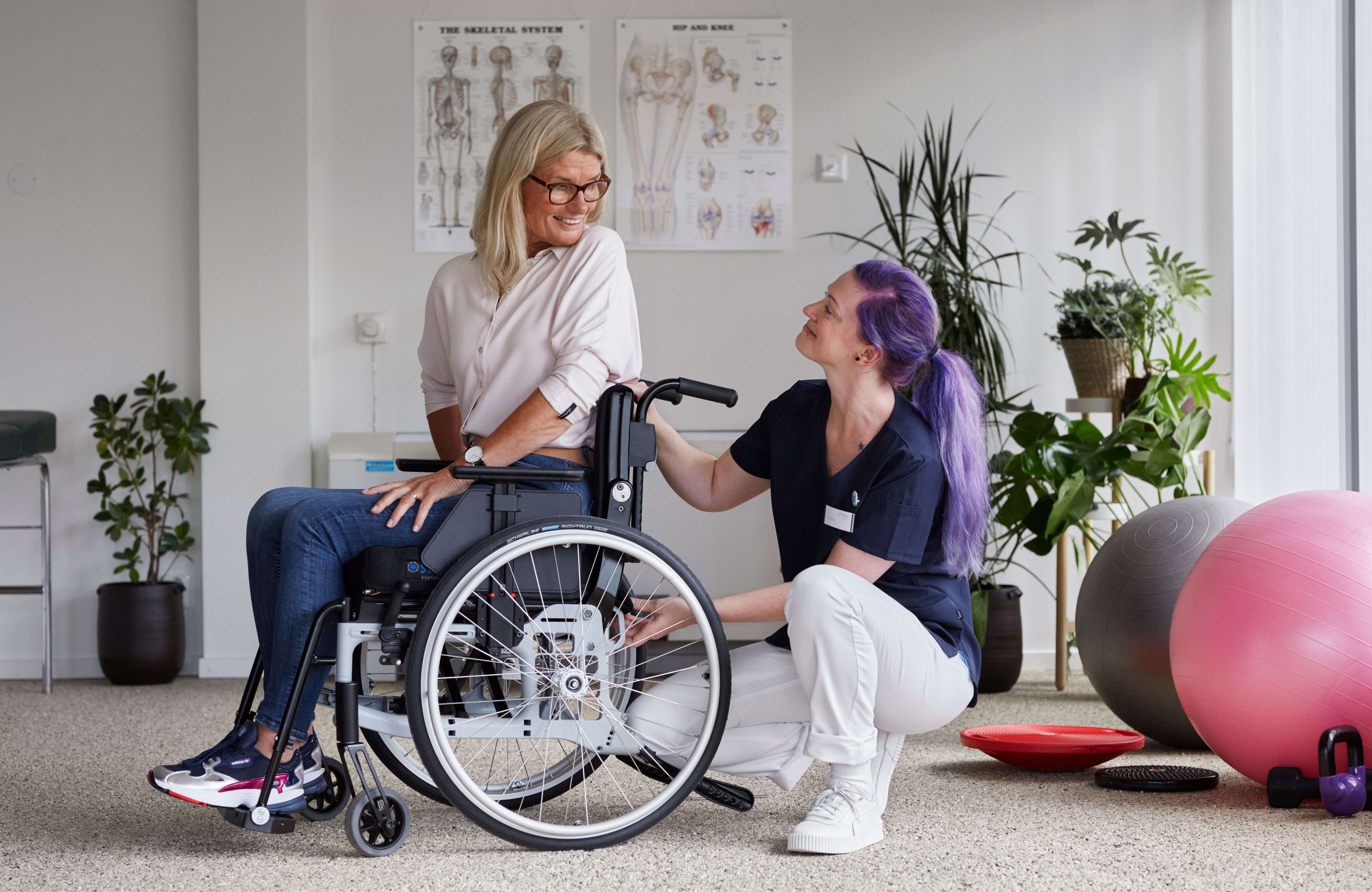 Person in a wheelchair being assisted by a caregiver in a rehabilitation setting.