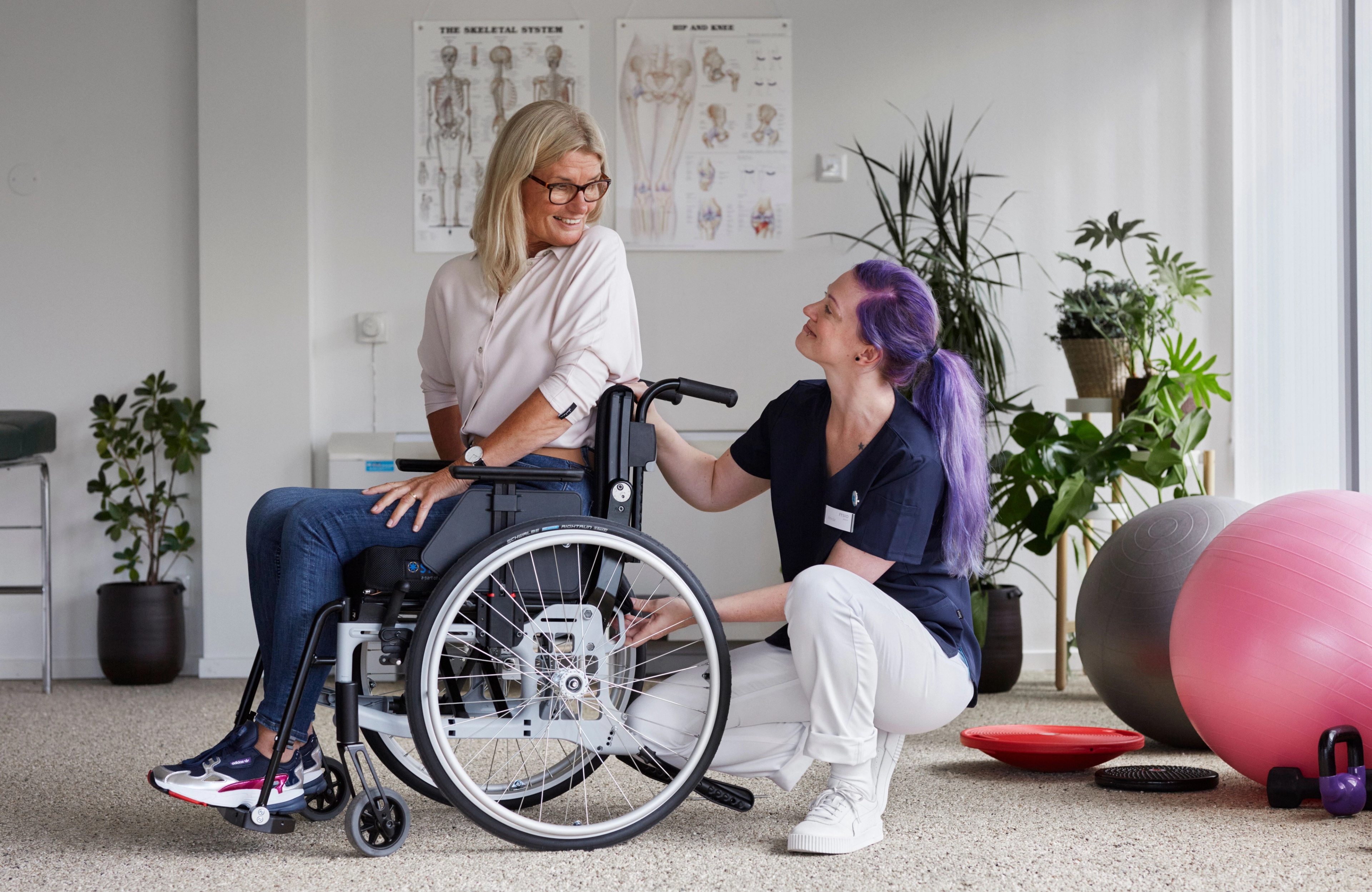Person in a wheelchair being assisted by a caregiver in a rehabilitation setting.