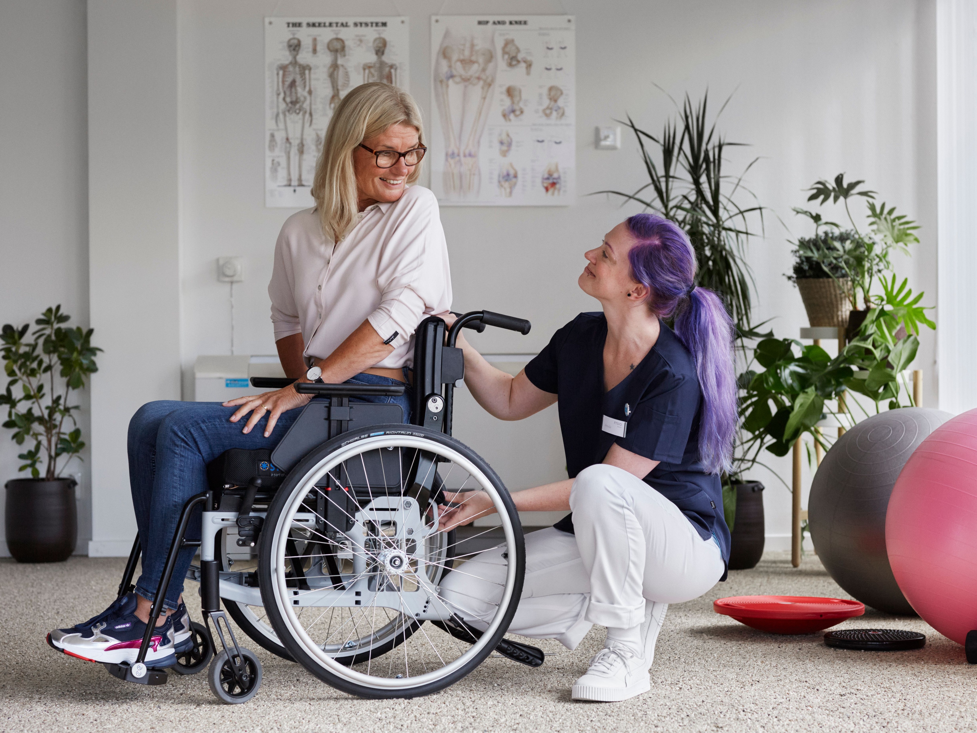 Person in a wheelchair being assisted by a caregiver in a rehabilitation setting.