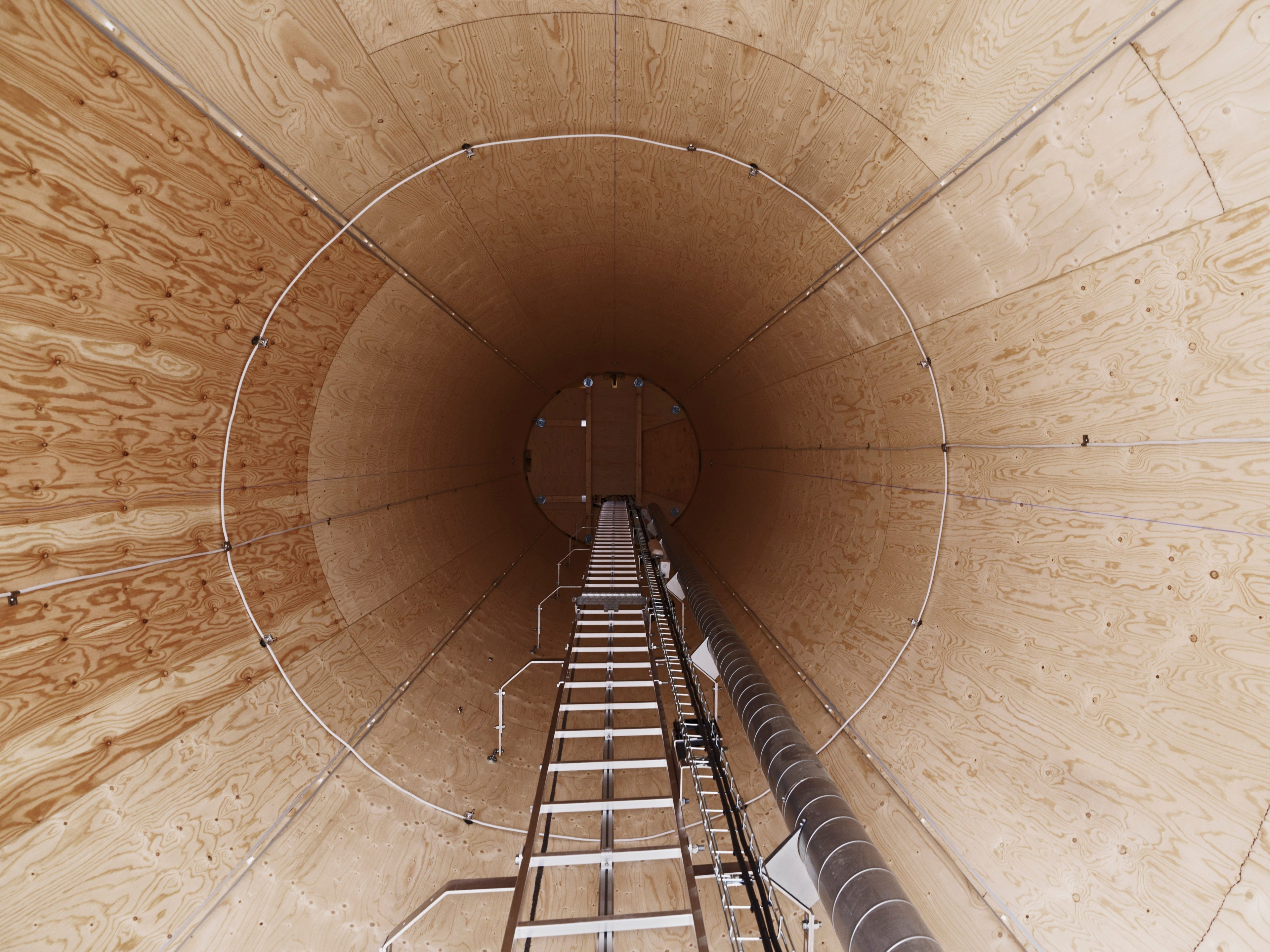 Interior of a tall wooden cylindrical structure with a ladder leading upward.