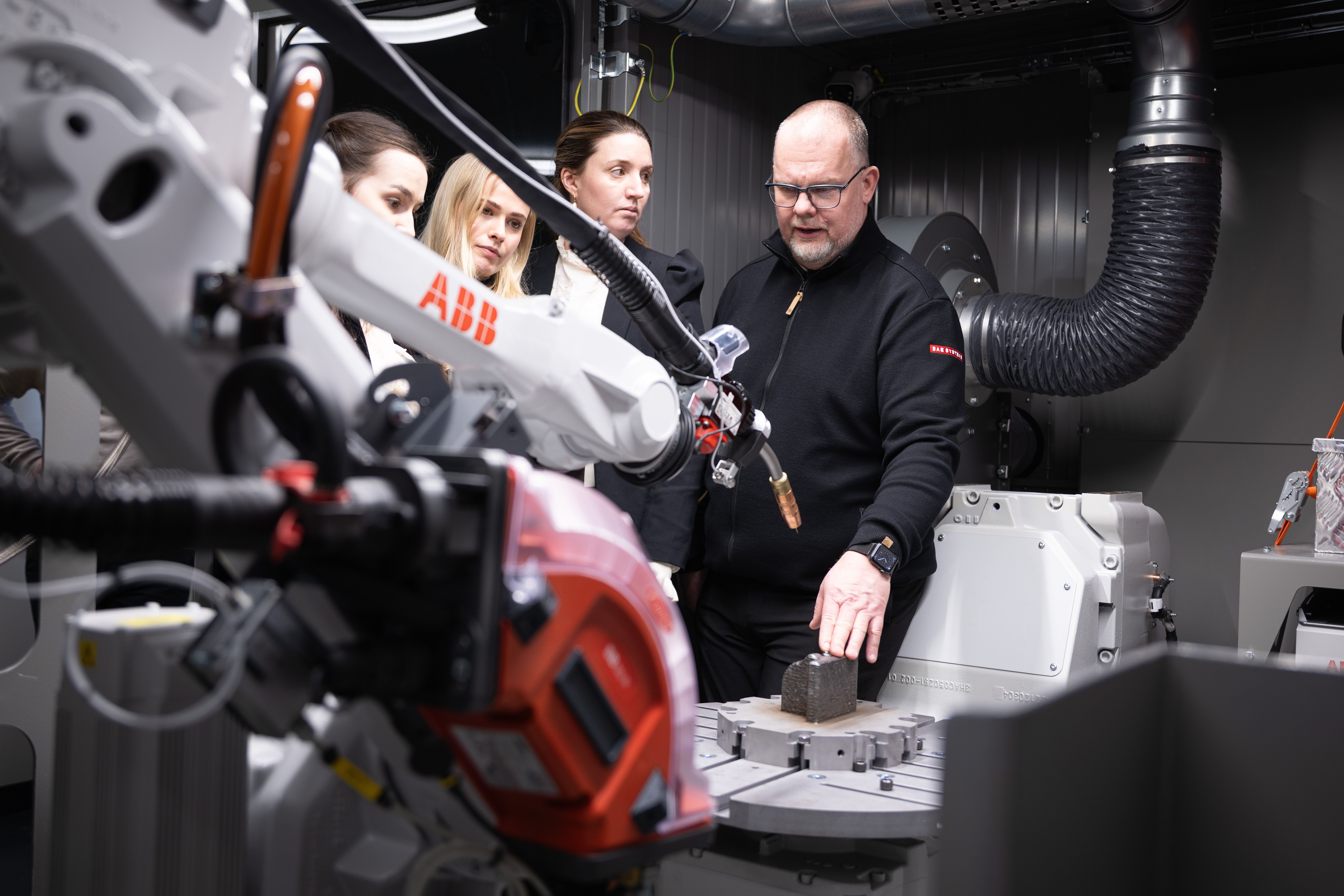 Engineers observing and working with an industrial robotic arm in a lab environment.