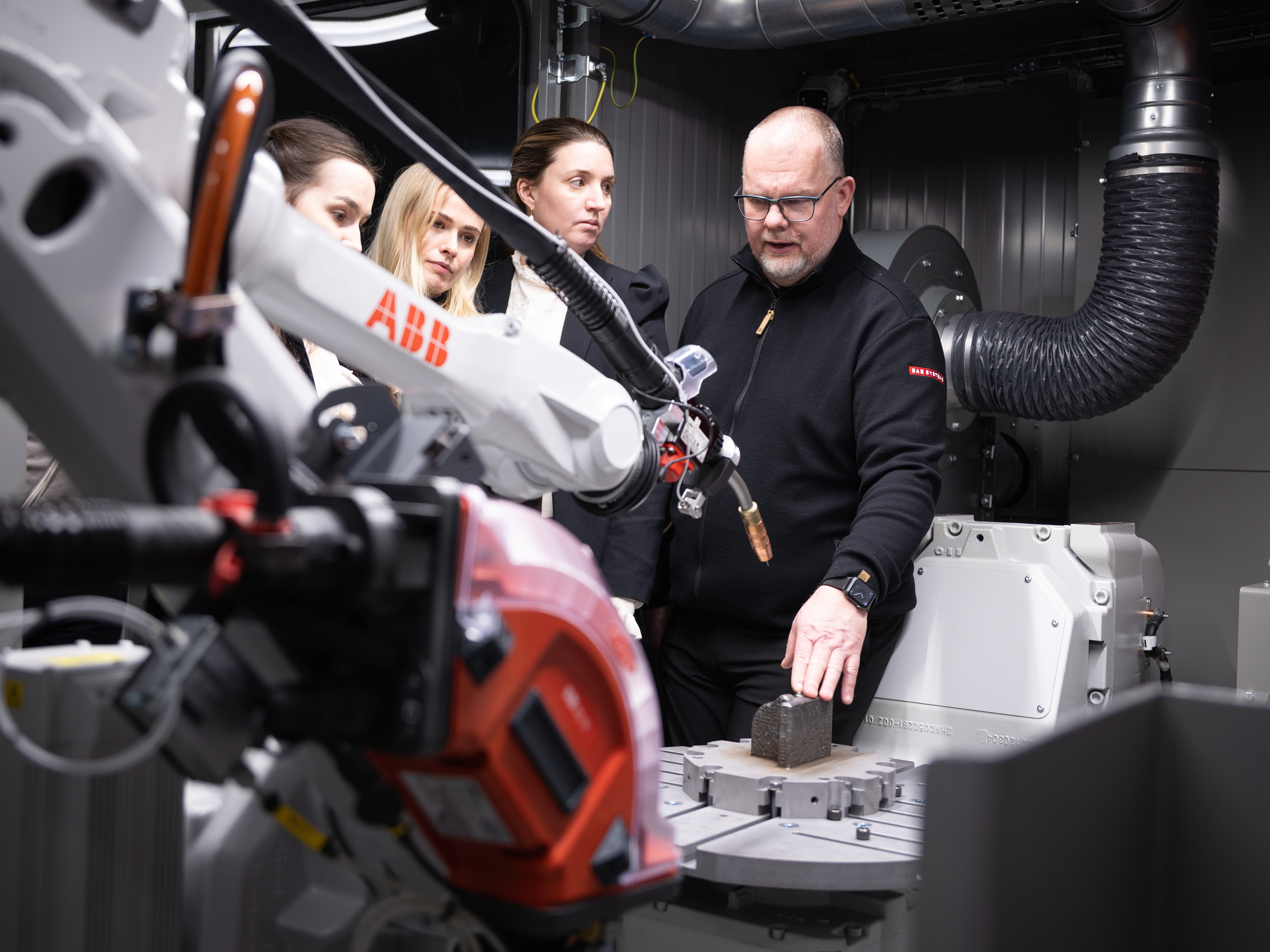 Engineers observing and working with an industrial robotic arm in a lab environment.