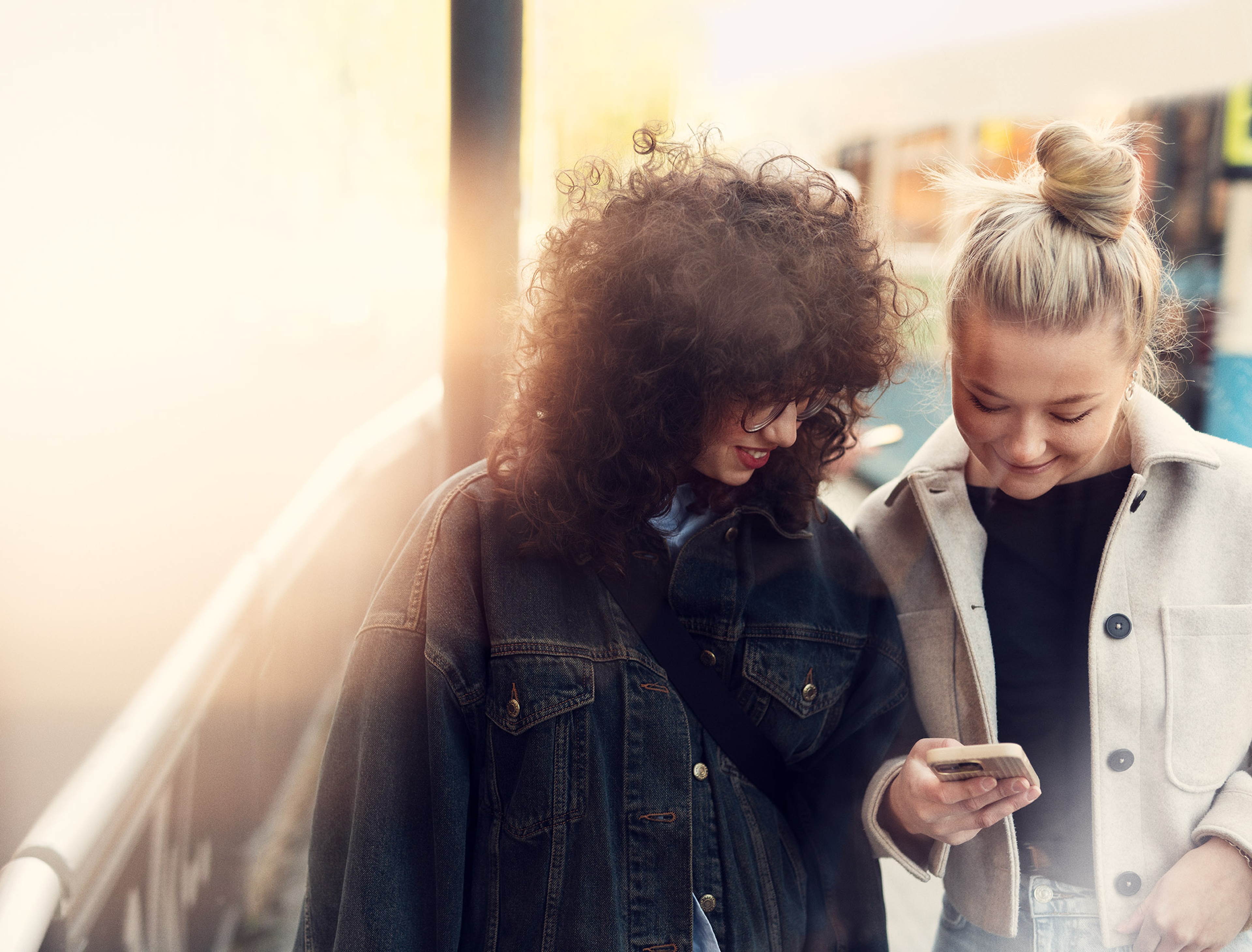 Two women walking beside each other in a city setting while looking at a mobile phone