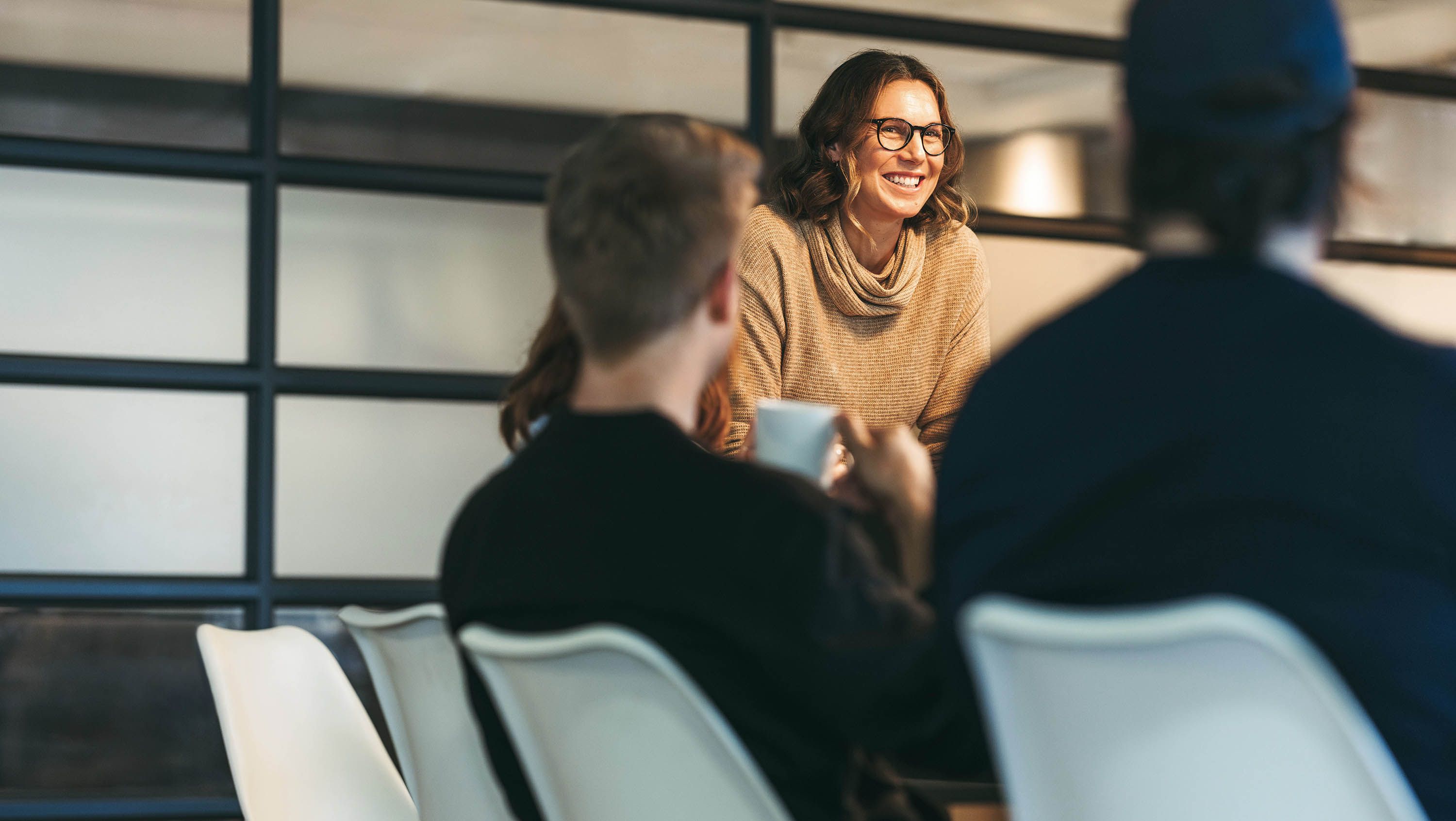 A woman standing at the edge of a conference table talking to the people sitting at the table